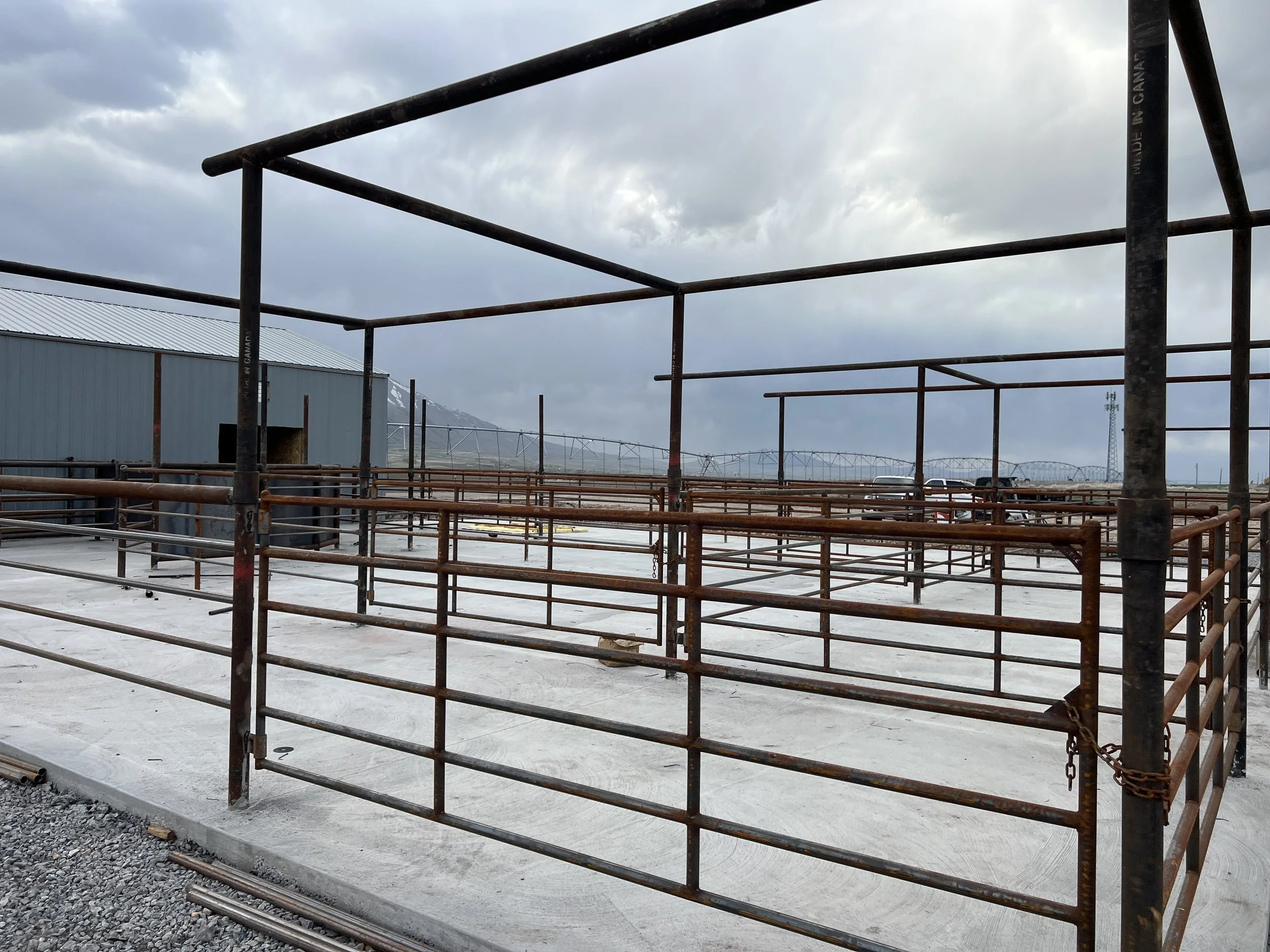 Construction site with rusted scaffolding around a concrete foundation, with mountains and a cloudy sky in the background.