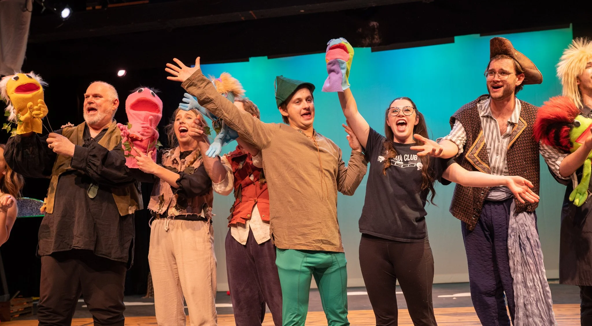 Group of people on stage wearing colorful costumes and puppets, celebrating or performing.