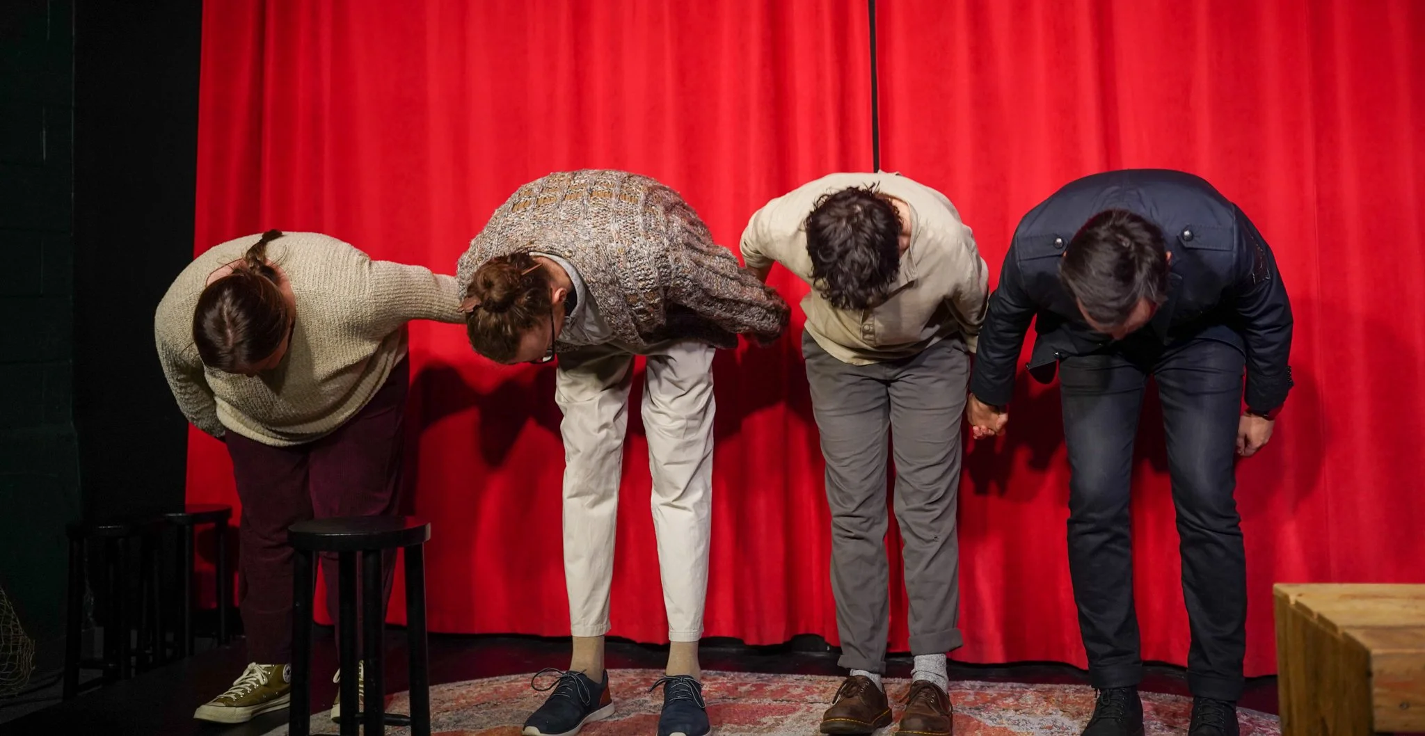Four people bowing on stage with a red curtain backdrop, holding hands.