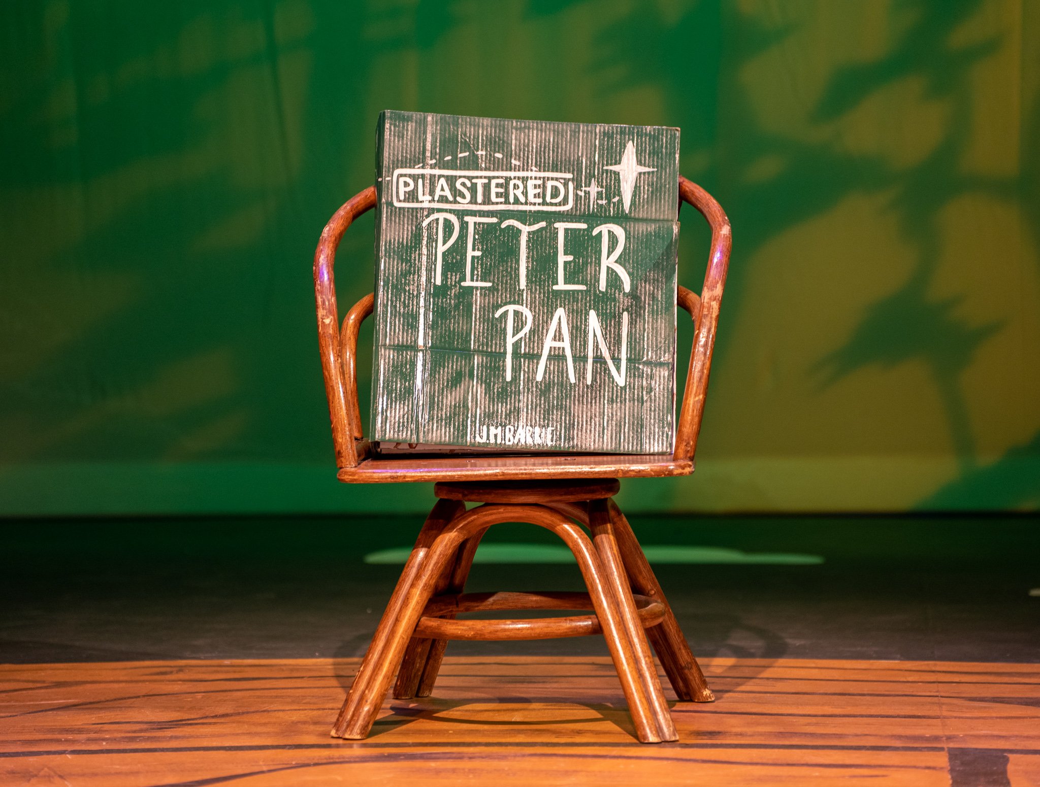 A wooden chair with a newspaper or magazine titled 'Pistered Peter Pan' resting on its backrest, set against a green and yellow background.