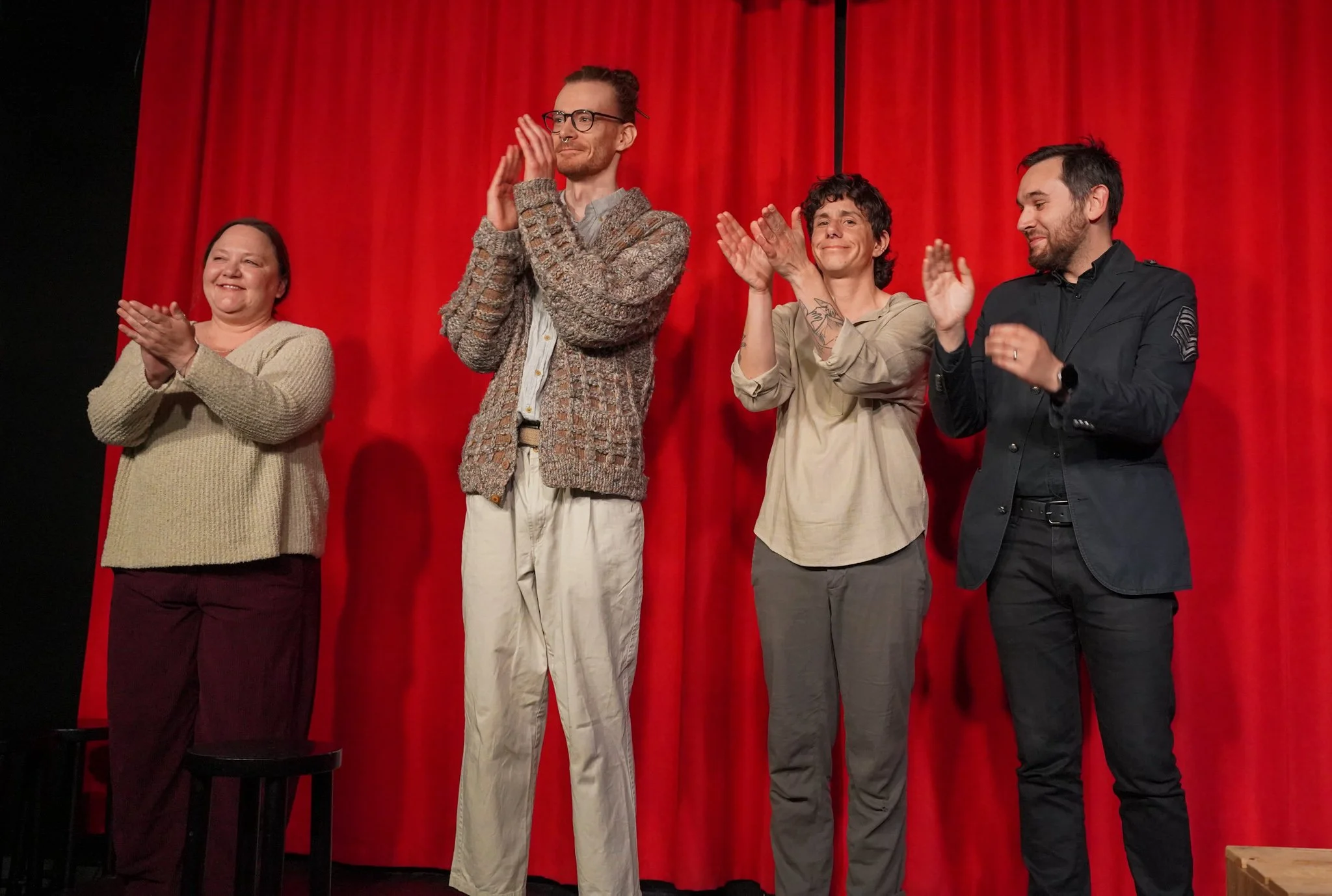 Four people standing in front of a red curtain, clapping and smiling.