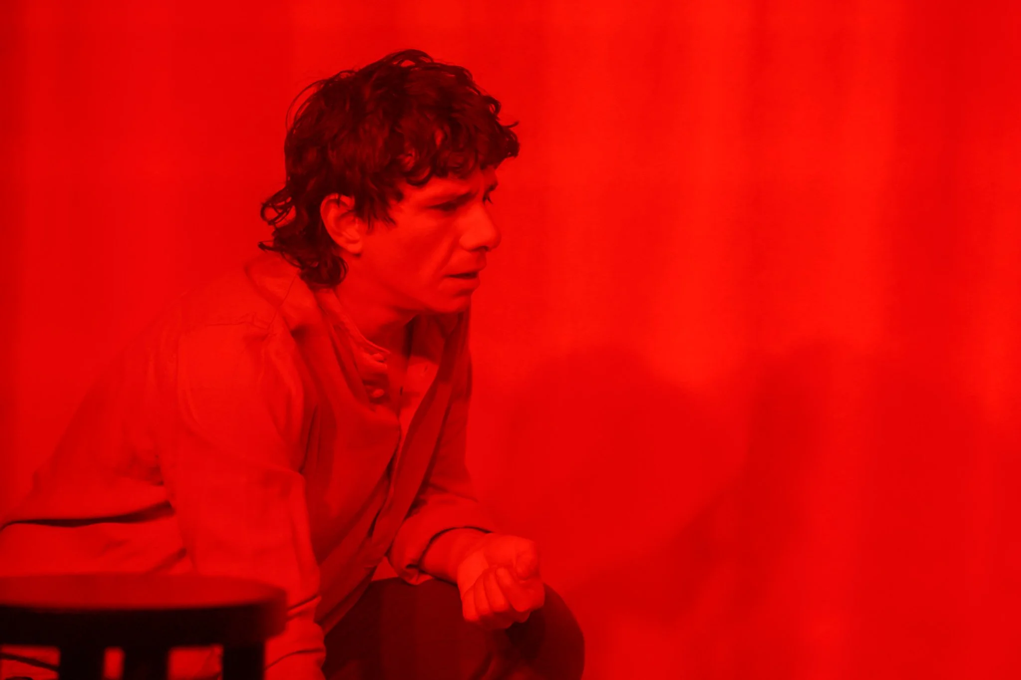 A person with curly hair wearing a jacket, sitting against a bright red background.