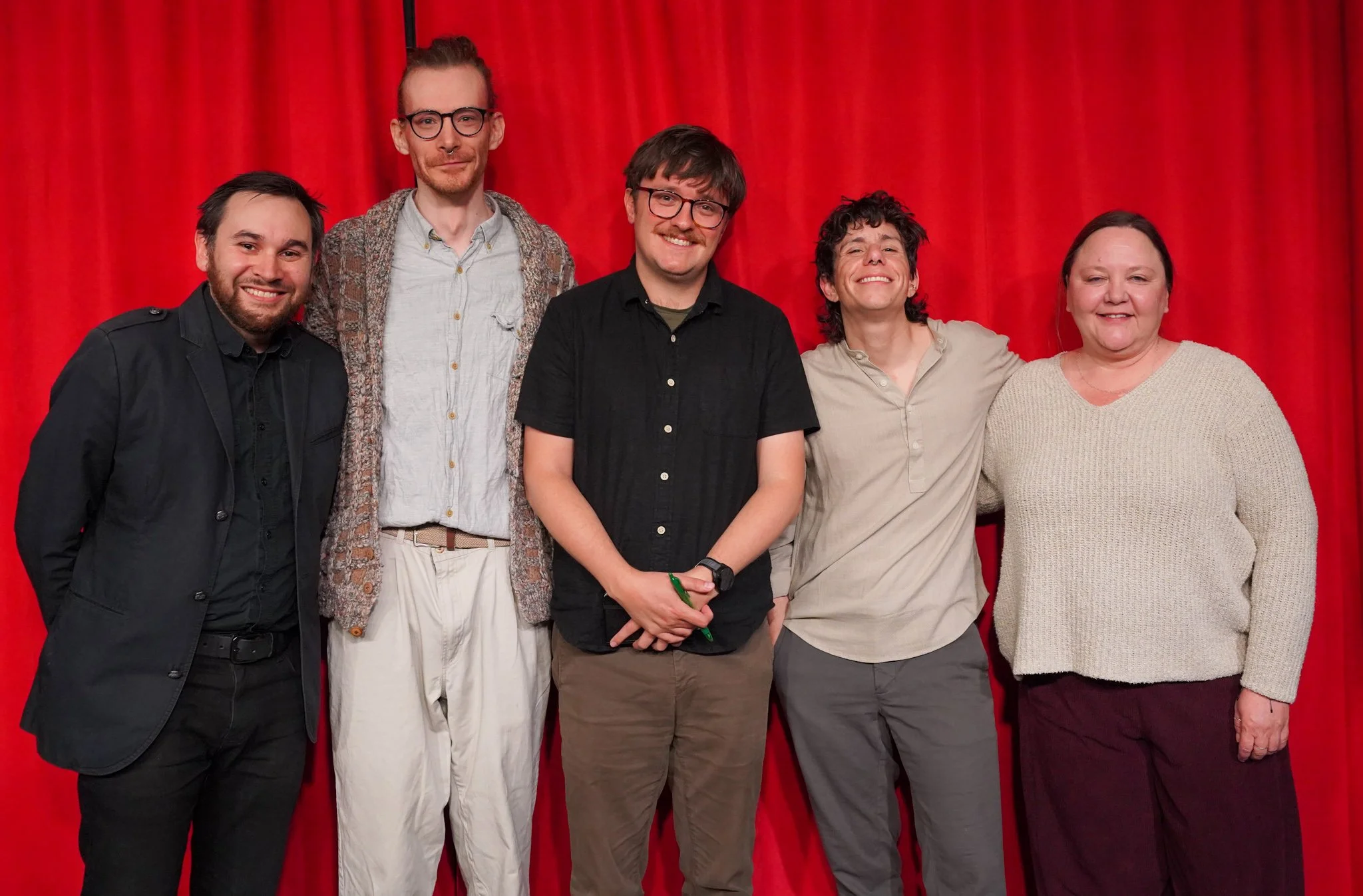 Group of five people standing in front of a red curtain, smiling for the photo.