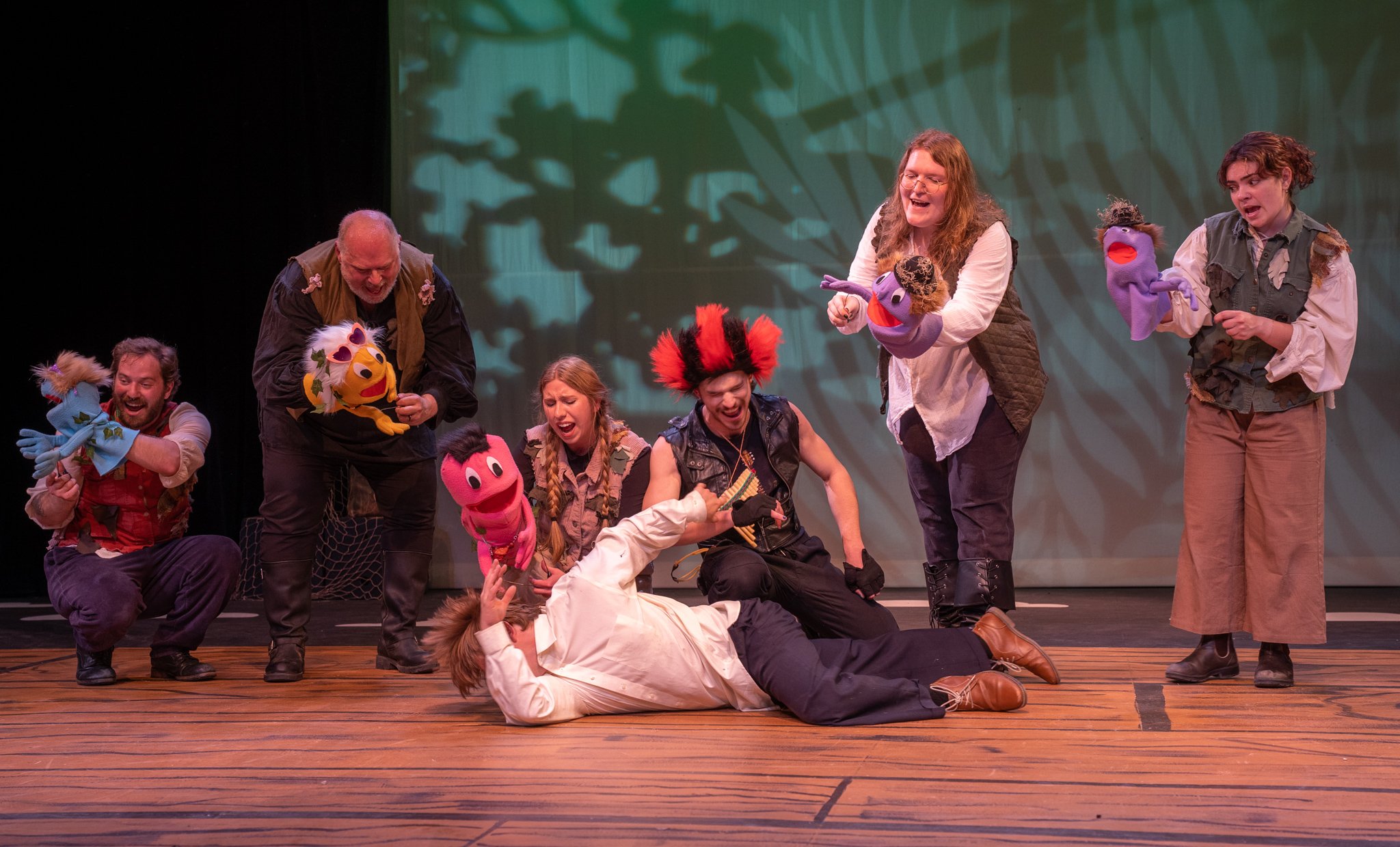 Theater performance with actors and puppets on stage, some actors are laughing and interacting with puppet characters.
