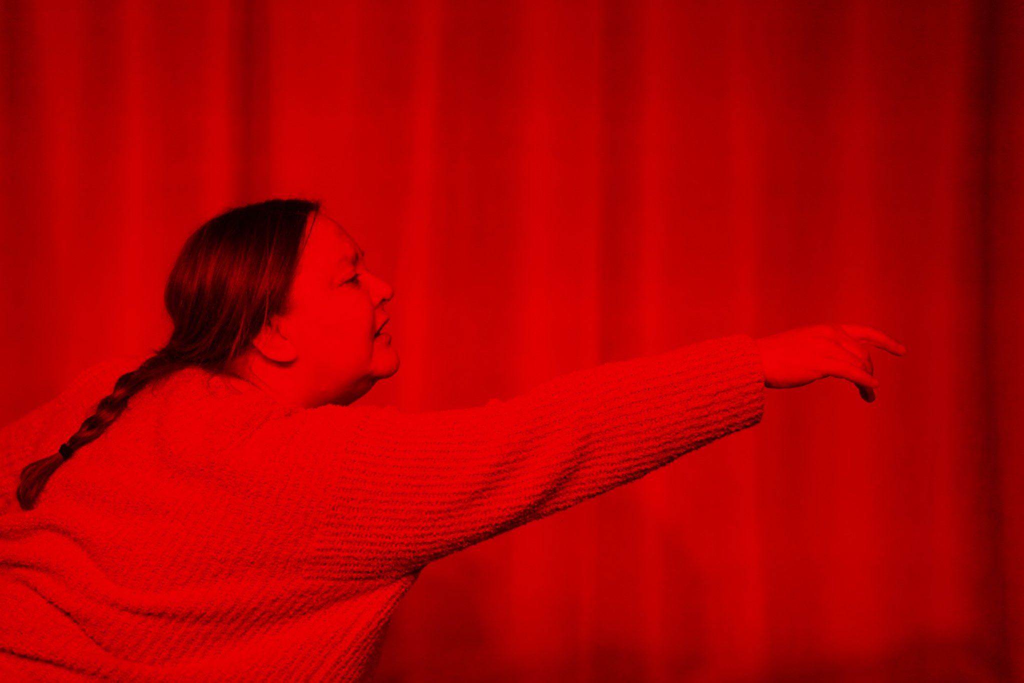 Person with braid reaching out against a red background.