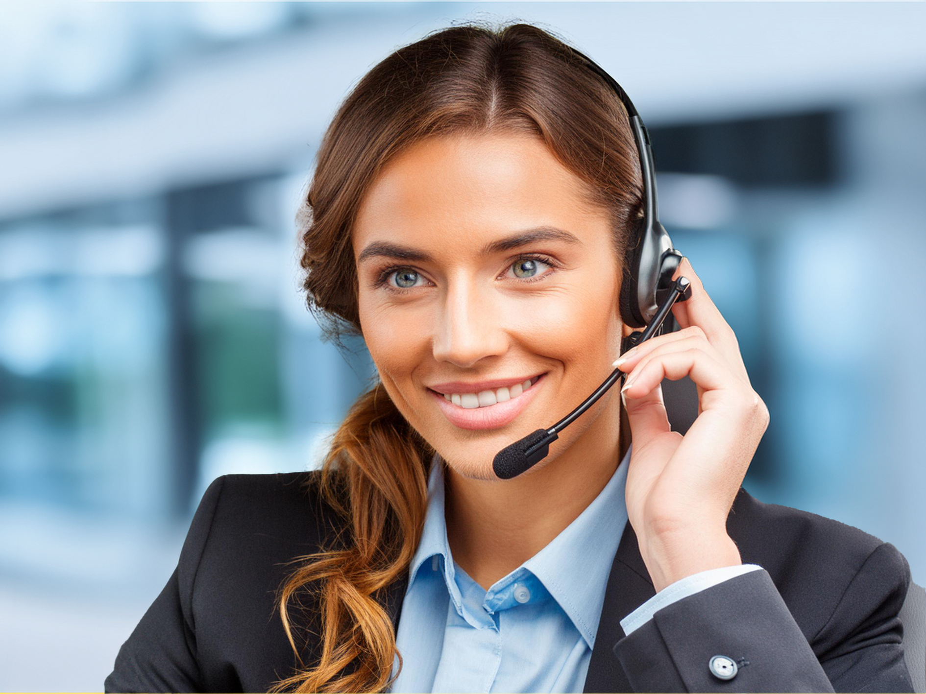 A smiling woman in business attire wearing a headset in an office setting.