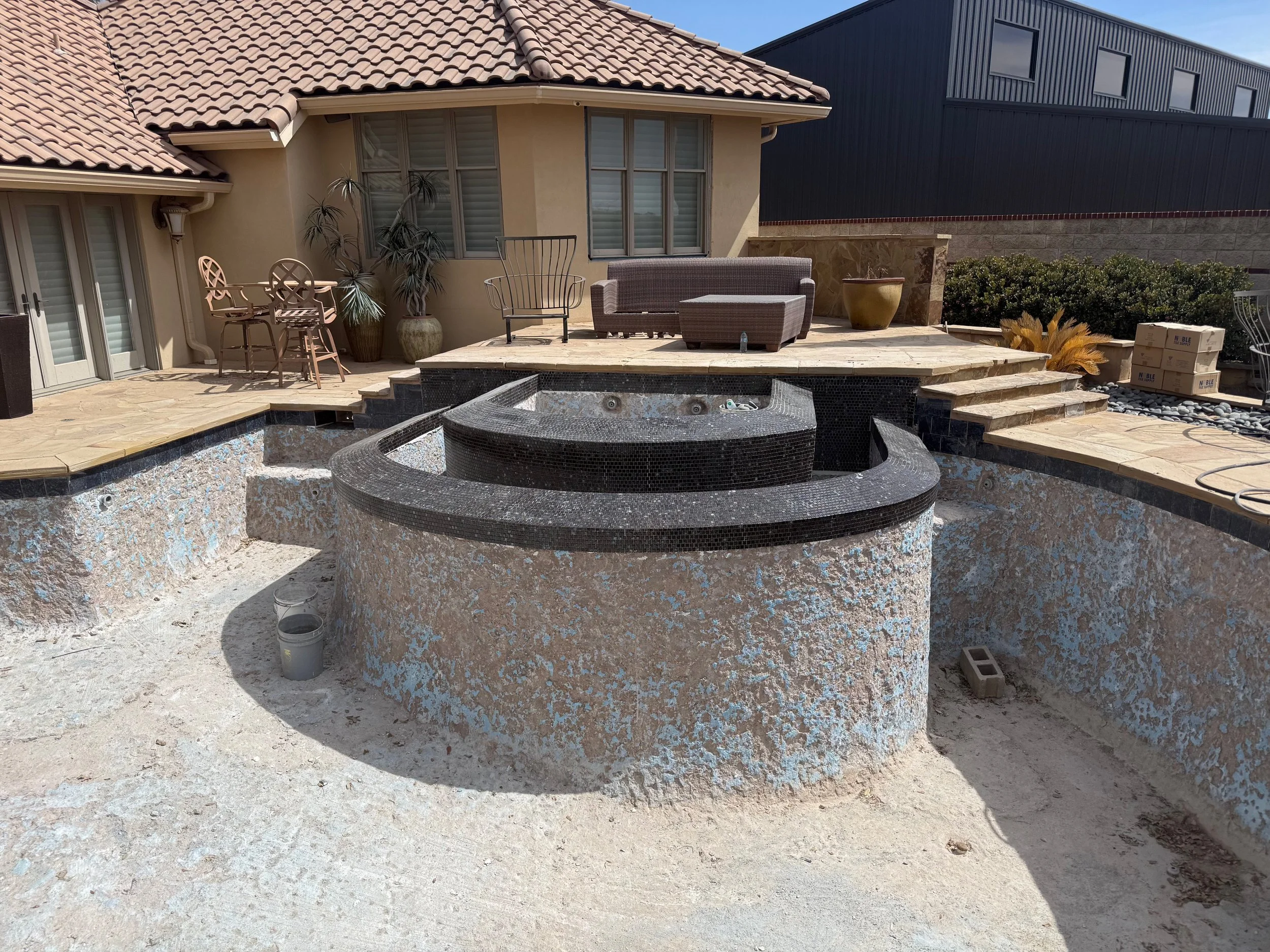 Backyard with a covered patio area featuring seating, potted plants, and an empty hot tub or pool with steps and construction debris around it.