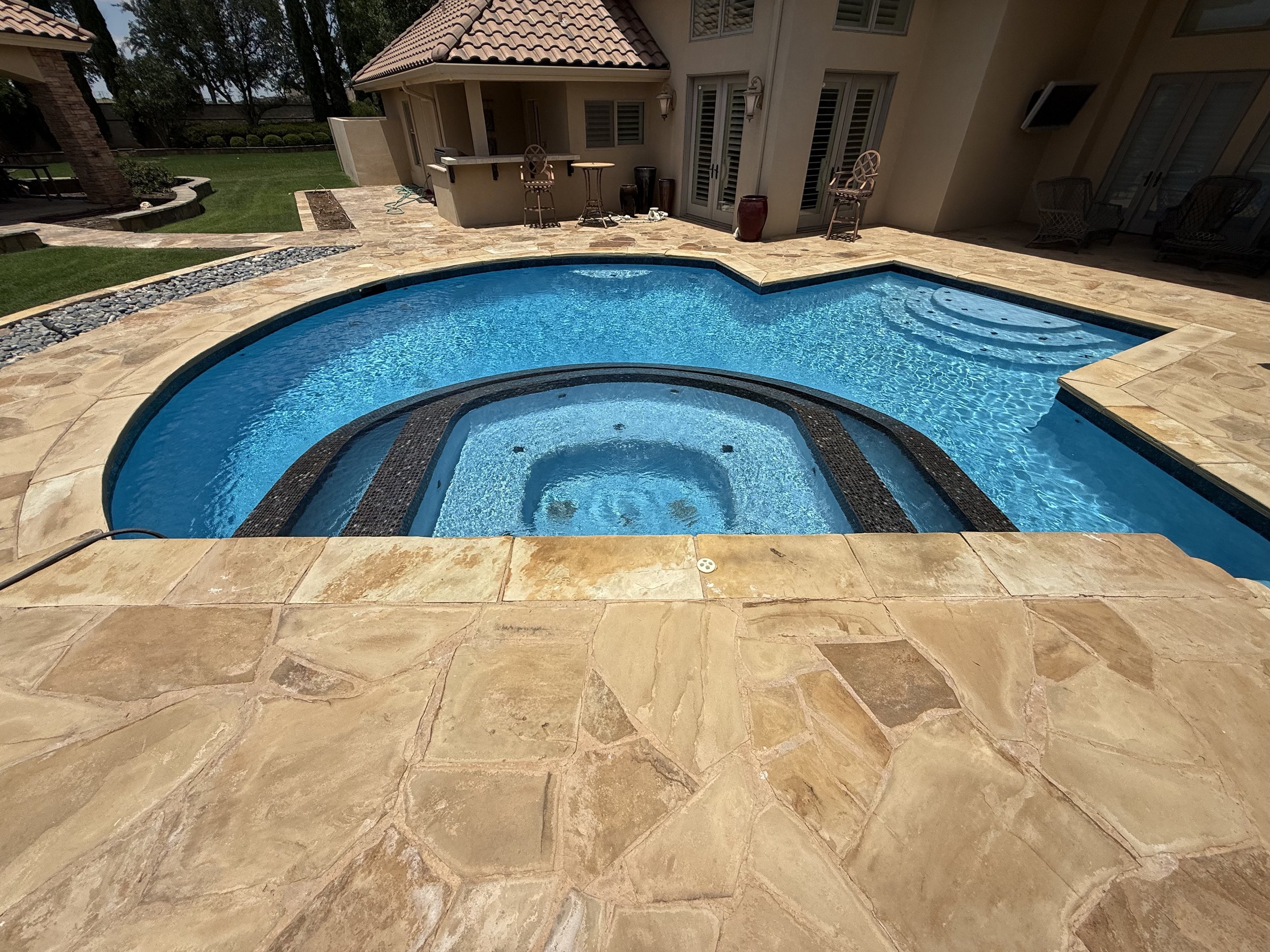 Backyard with pool, patio, outdoor furniture, and a house with windows and shutters.