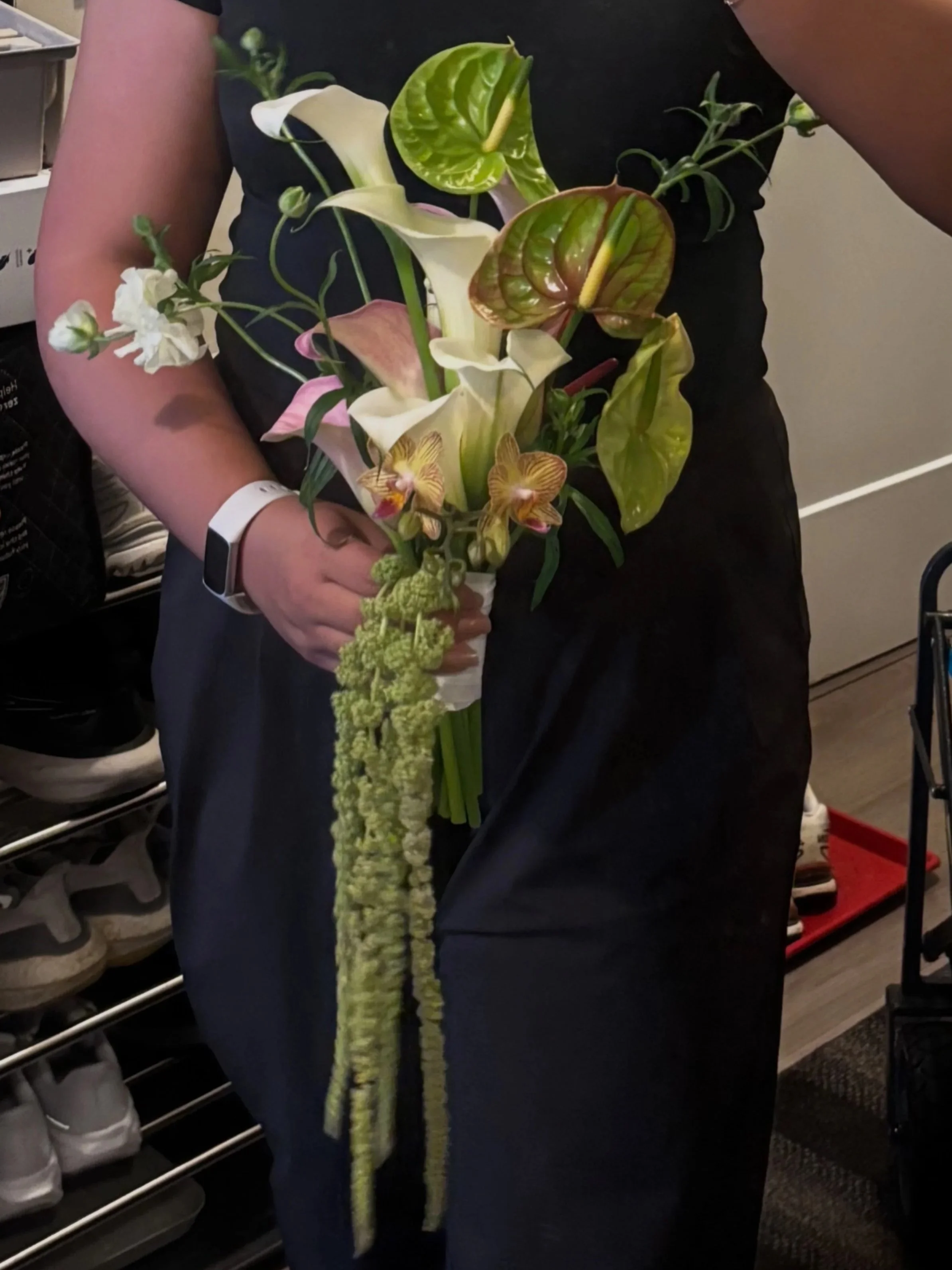 Person holding a bouquet of various flowers including calla lilies, anthuriums, orchids, and green foliage.