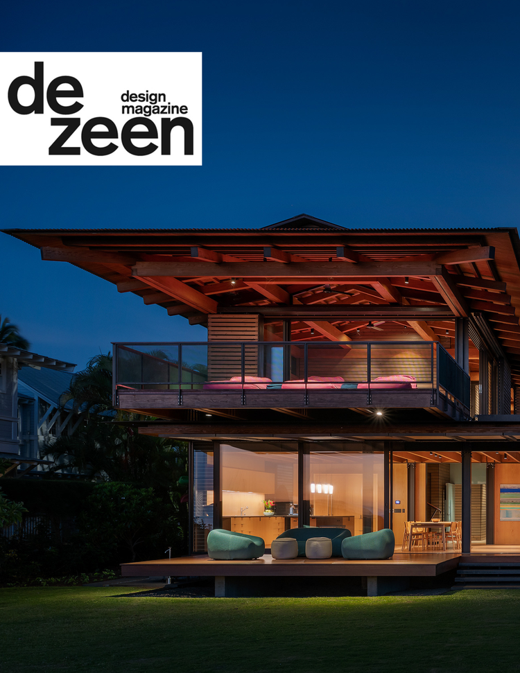 Modern two-story house with large glass windows, wooden exterior, and an illuminated interior at dusk, featuring outdoor seating on a wooden deck and a balcony.