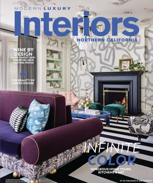 Cover of Modern Luxury Interiors magazine featuring a modern living room with a purple velvet sofa, decorative pillows, a fireplace, and artistic wall design.