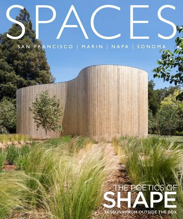 A modern, curved wooden building surrounded by grass and trees, under a clear blue sky, on the cover of a magazine titled 'SPACES'.