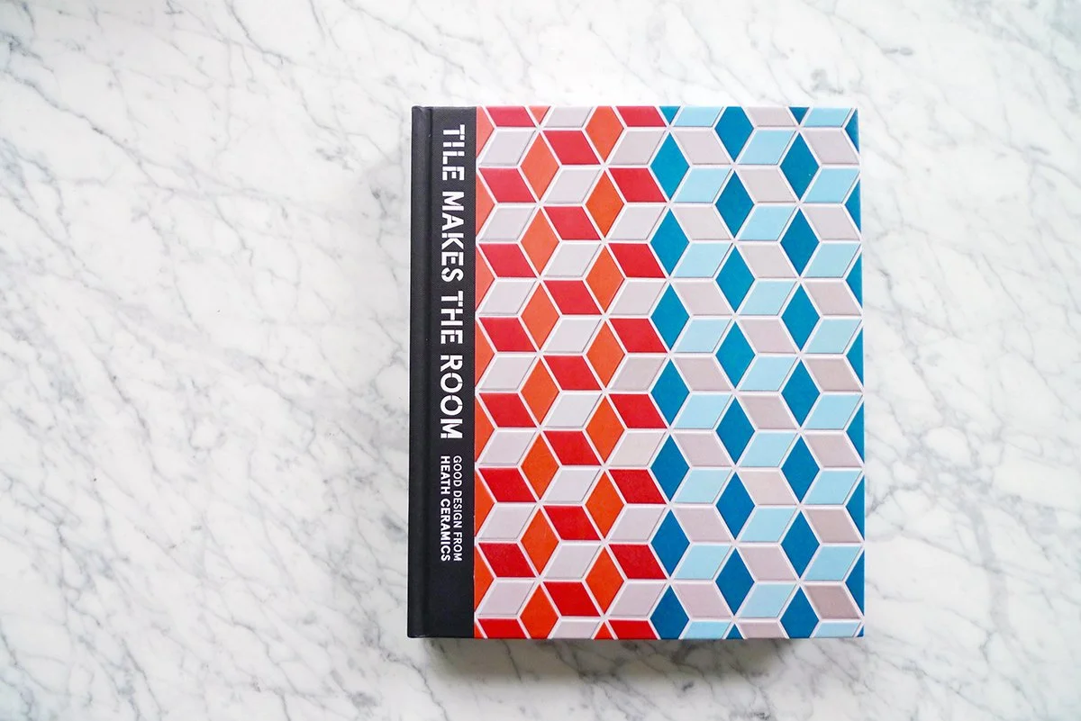 Book titled "The Makes the Room" with a colorful geometric pattern on the cover, placed on a white marble surface.
