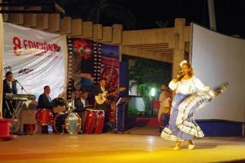 Group of musicians playing drums and guitar on stage with a dancer performing in front.