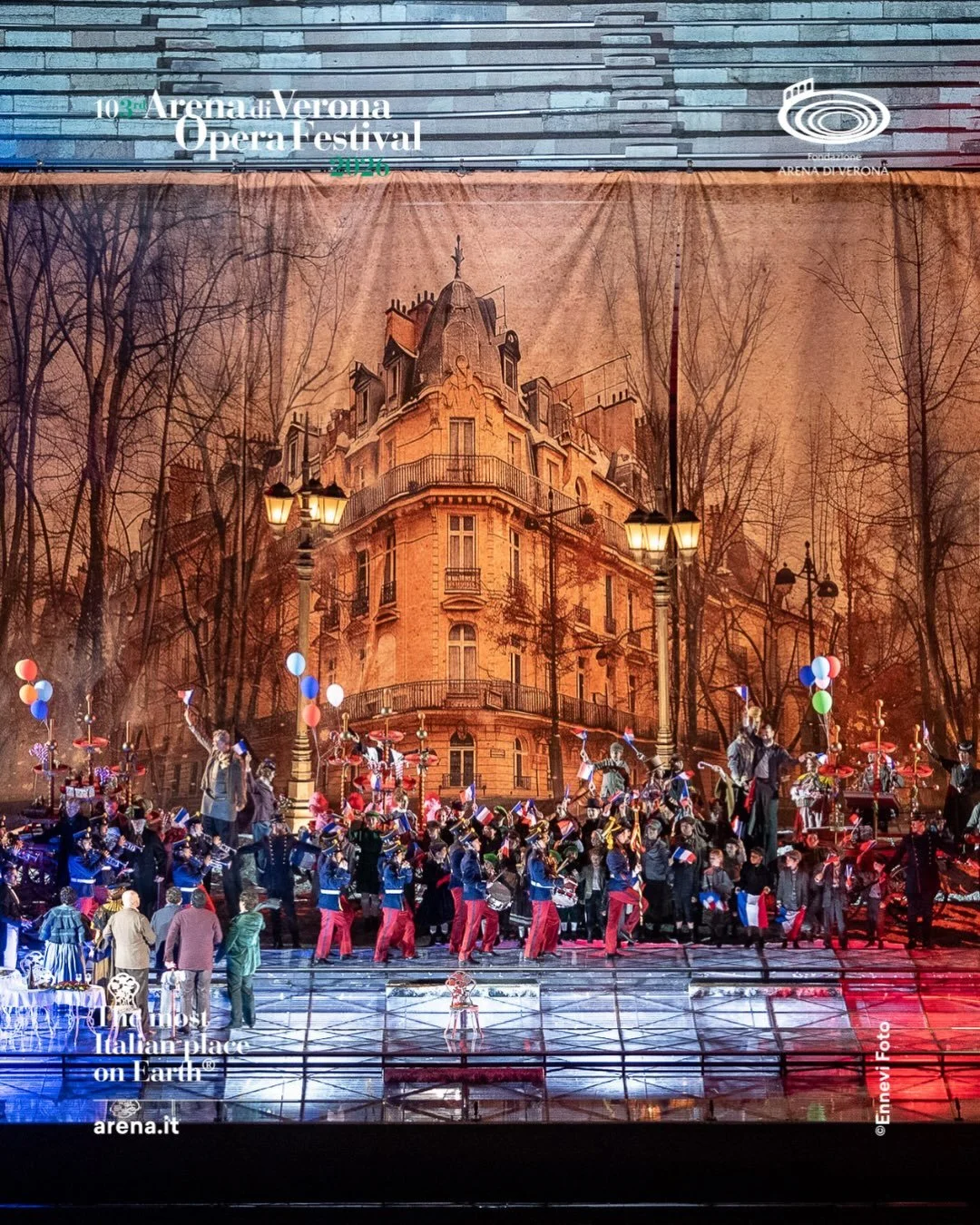 Scena di un'opera teatrale durante il Verona Opera Festival con attori e orchestrali sul palco, sfondo di un edificio con decorazioni di stile parigino e atmosfera autunnale.