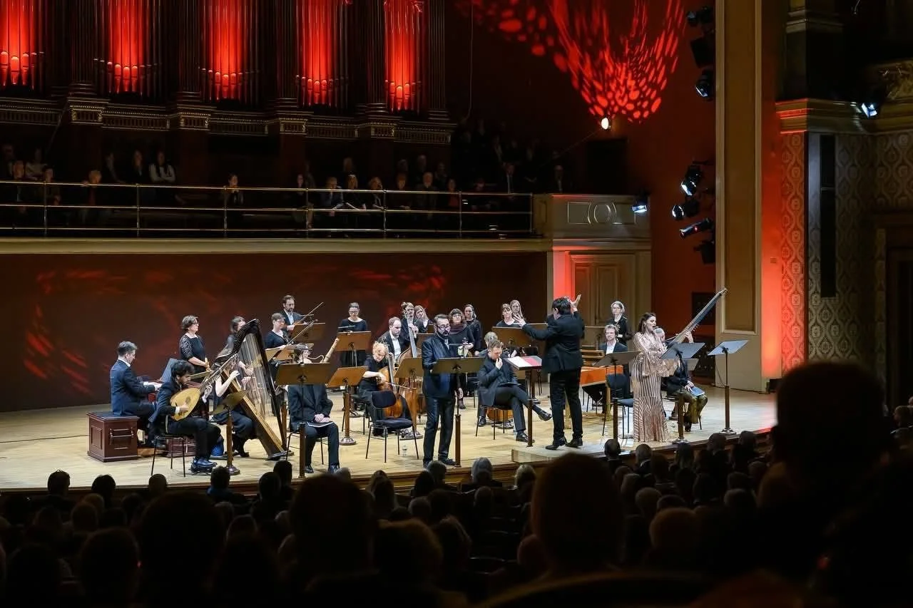 Orchestra durante un concerto in un teatro, con un pubblico seduto e un direttore d'orchestra che dirige i musicisti.