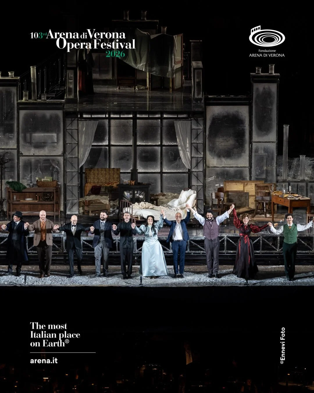 Immagine del cast di un'opera teatrale sul palco, con uno sfondo che rappresenta una scena di casa con mobili e un letto, e in primo piano attori che si tengono per mano, celebrando lo spettacolo. In alto a sinistra viene annunciato il 3° Festival Op