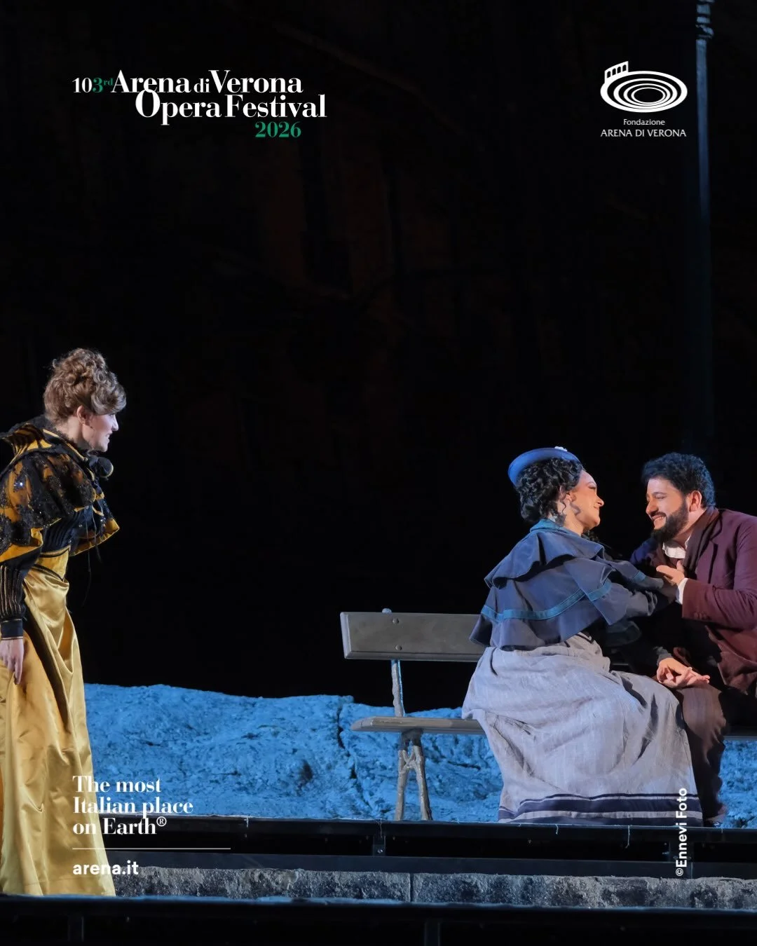 Tre attori sulla scena di un'opera al Teatro Arena di Verona. Due di loro sono seduti su una panchina, mentre una altra si avvicina. La scena ha un'illuminazione teatrale.