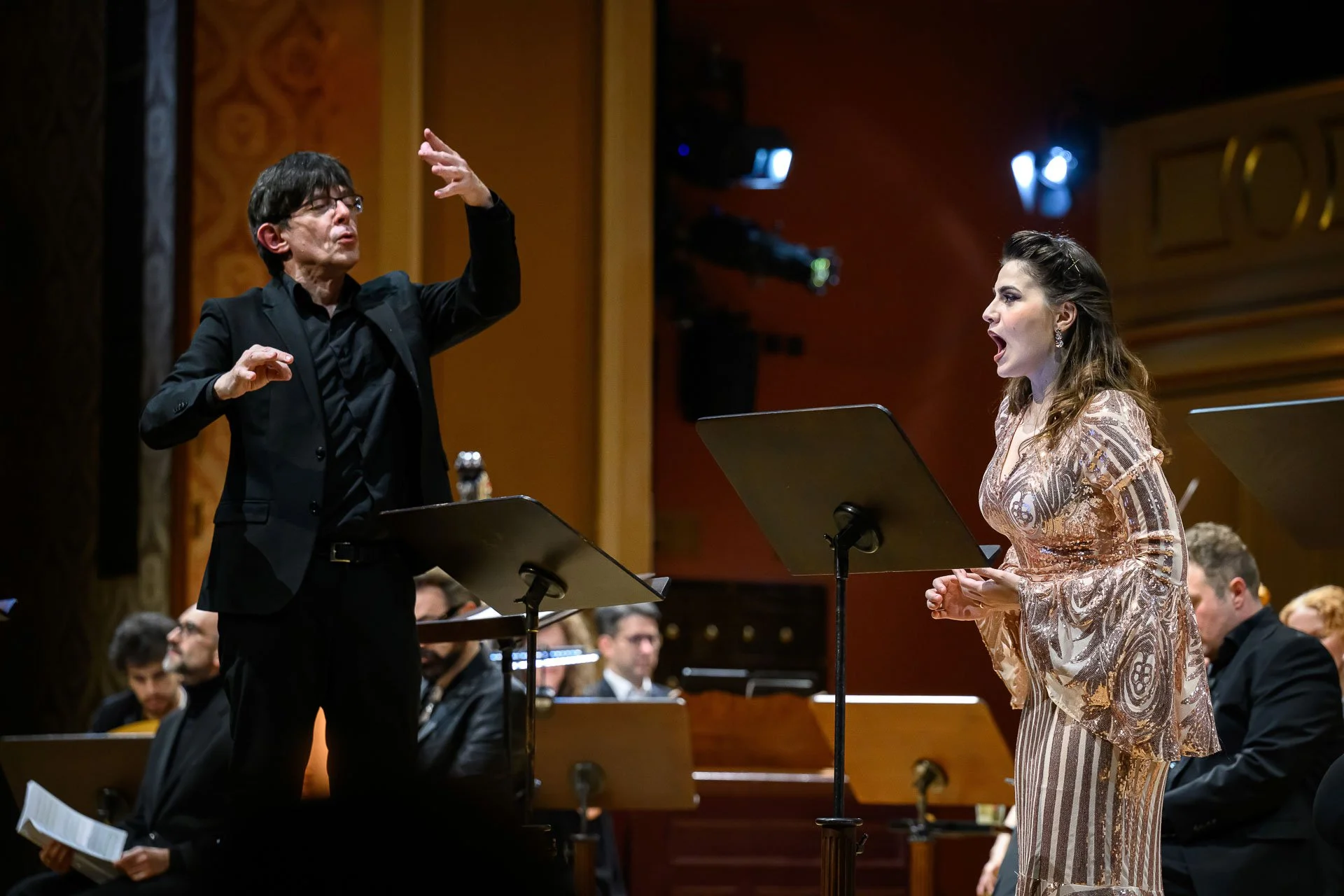 Direttore d'orchestra e cantante in concerto, con un coro e orchestra sul palcoscenico di un teatro.