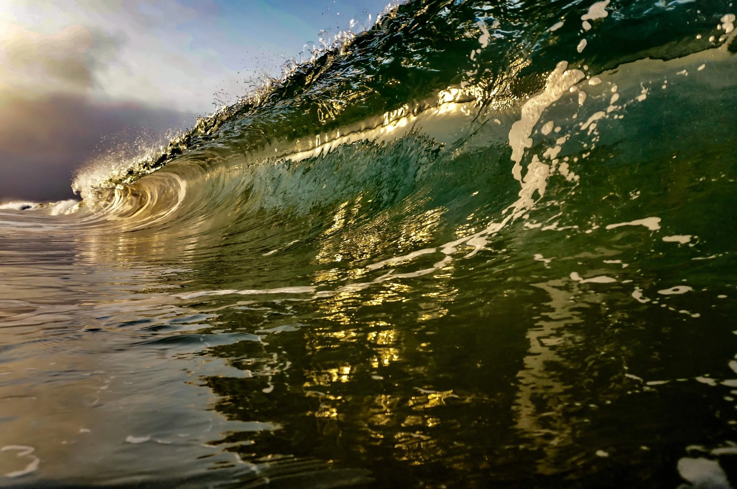 A close-up of a small ocean wave with sunlight reflecting on the water, as seen from underwater.