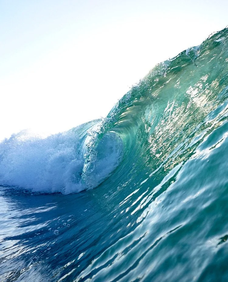 A large ocean wave with clear blue-green water, cresting and curling over.