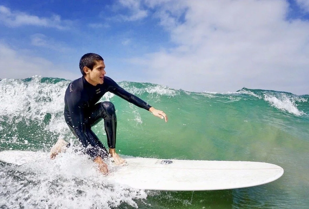 A person in a black wetsuit surfing on a white surfboard on a partly cloudy day with blue skies and green ocean waves.