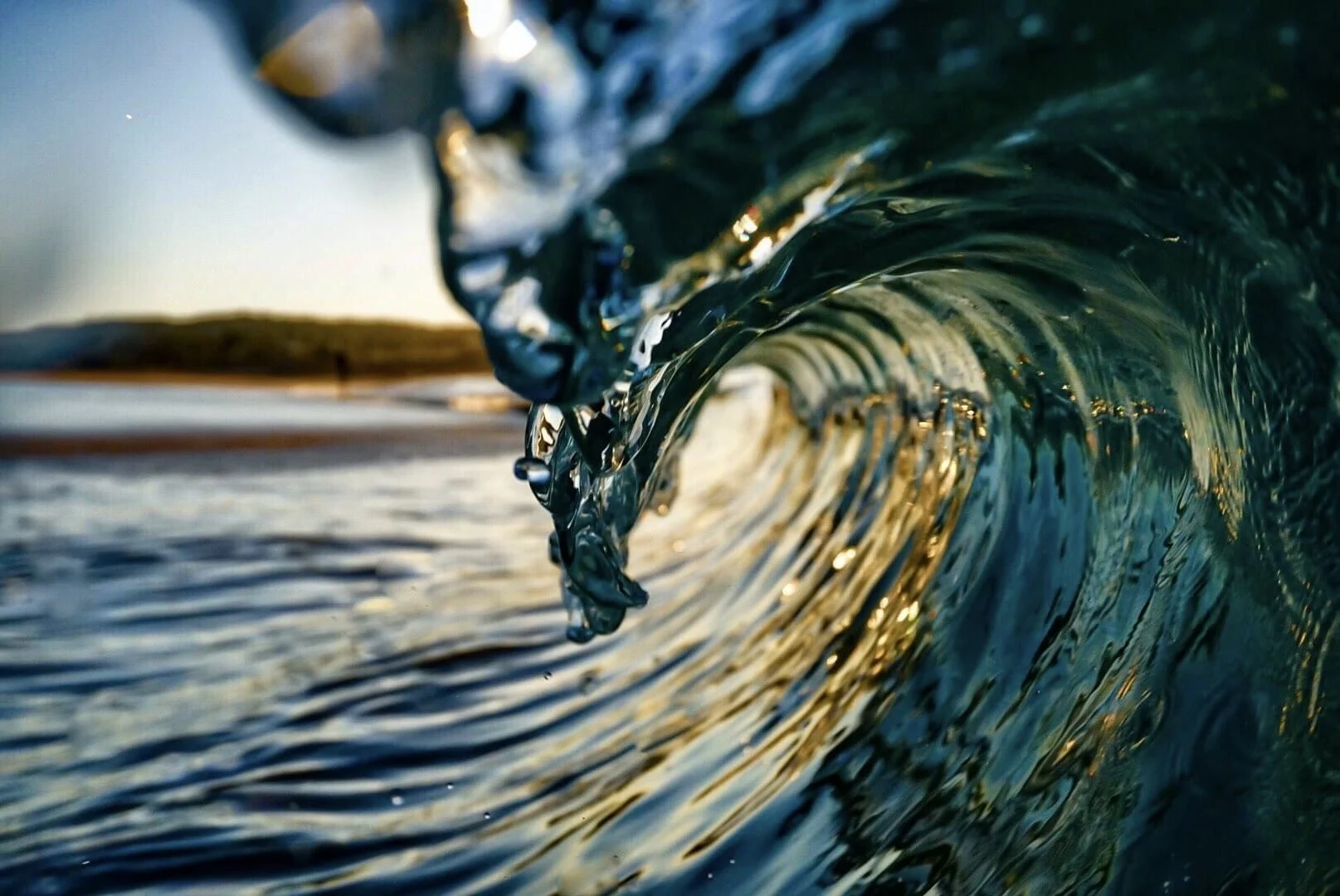 Close-up of an ocean wave curling as it approaches the shore during sunset or sunrise.