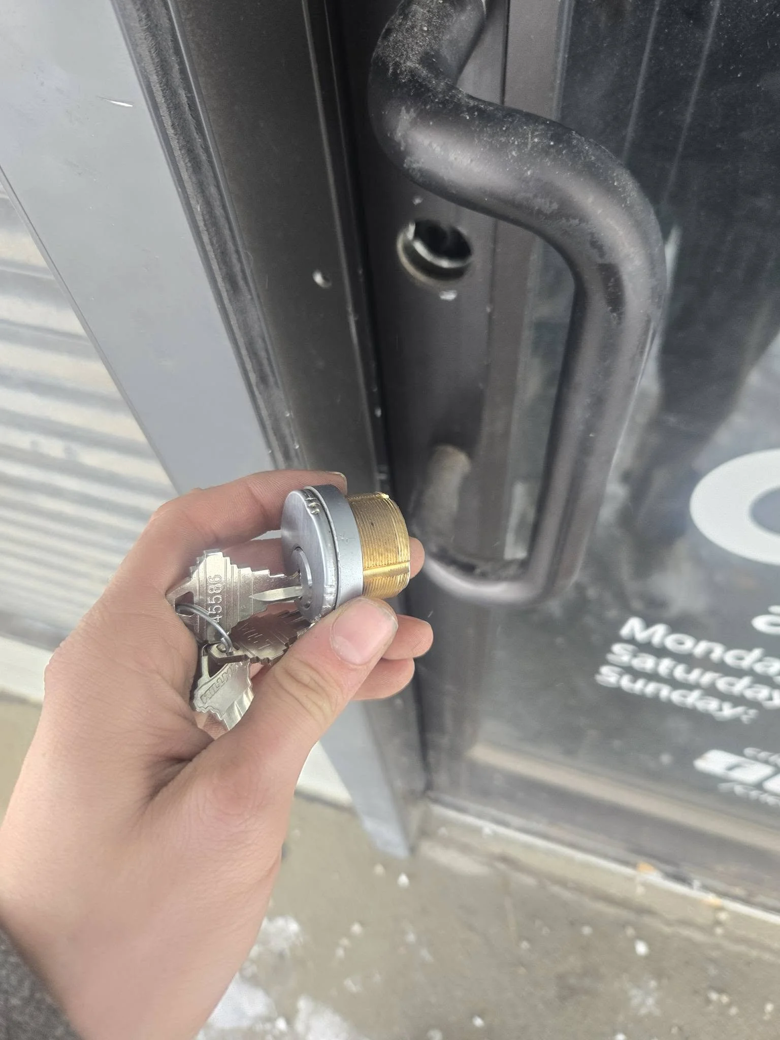 A person holding a lock and key near a door latch on a metal door with a sign that reads 'Mercedes-Benz Sicherheits Schließer'.