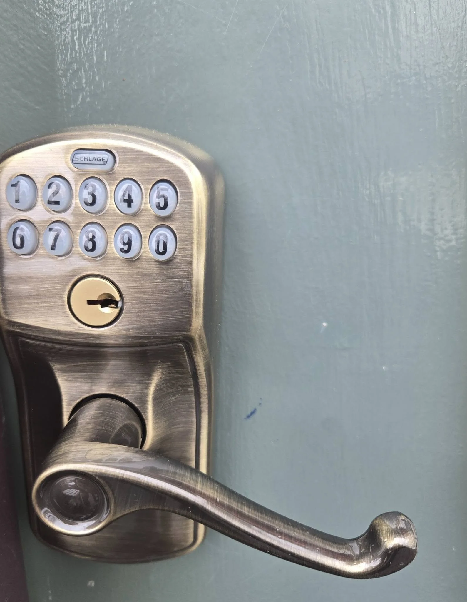 A metallic door lock with a keypad, reading 'Schlage', mounted on a metallic surface.
