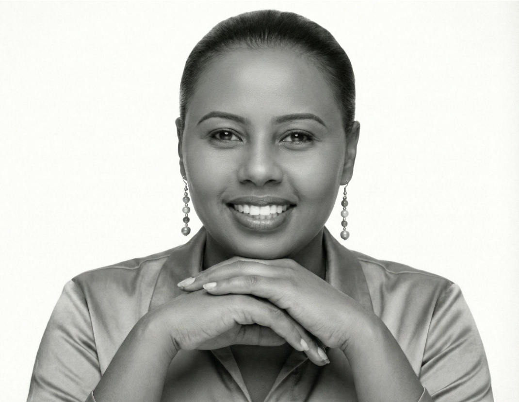 Black and white portrait of a woman smiling with hands clasped under her chin, wearing earrings and a satin blouse.