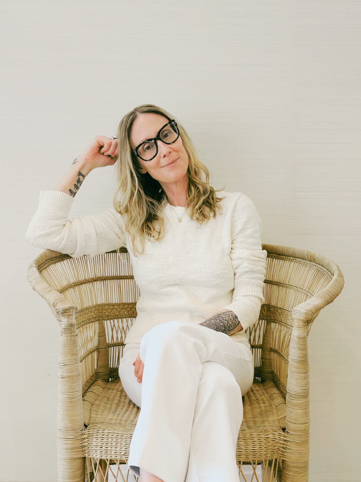 Kelly Chapman, LCSW, seated in a woven rattan chair against a light wall.