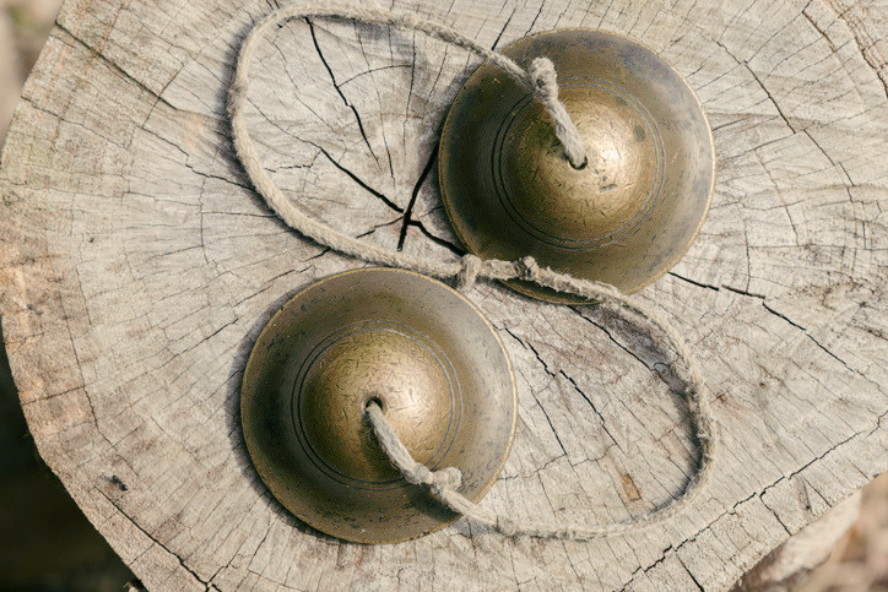 Two small brass cymbals joined by a cord, resting on a cracked wood surface.