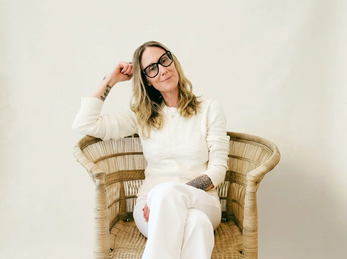 Kelly Chapman, LCSW, seated in rattan chair with head tilted and resting on hand.