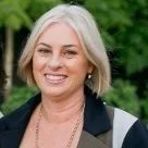 A smiling woman with short gray hair outdoors with green foliage in the background.