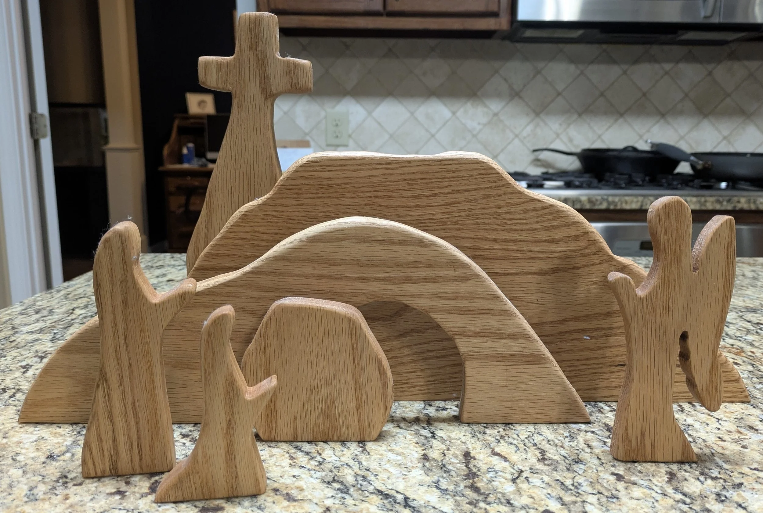 Set of wooden figurines arranged on a countertop, with a kitchen in the background.