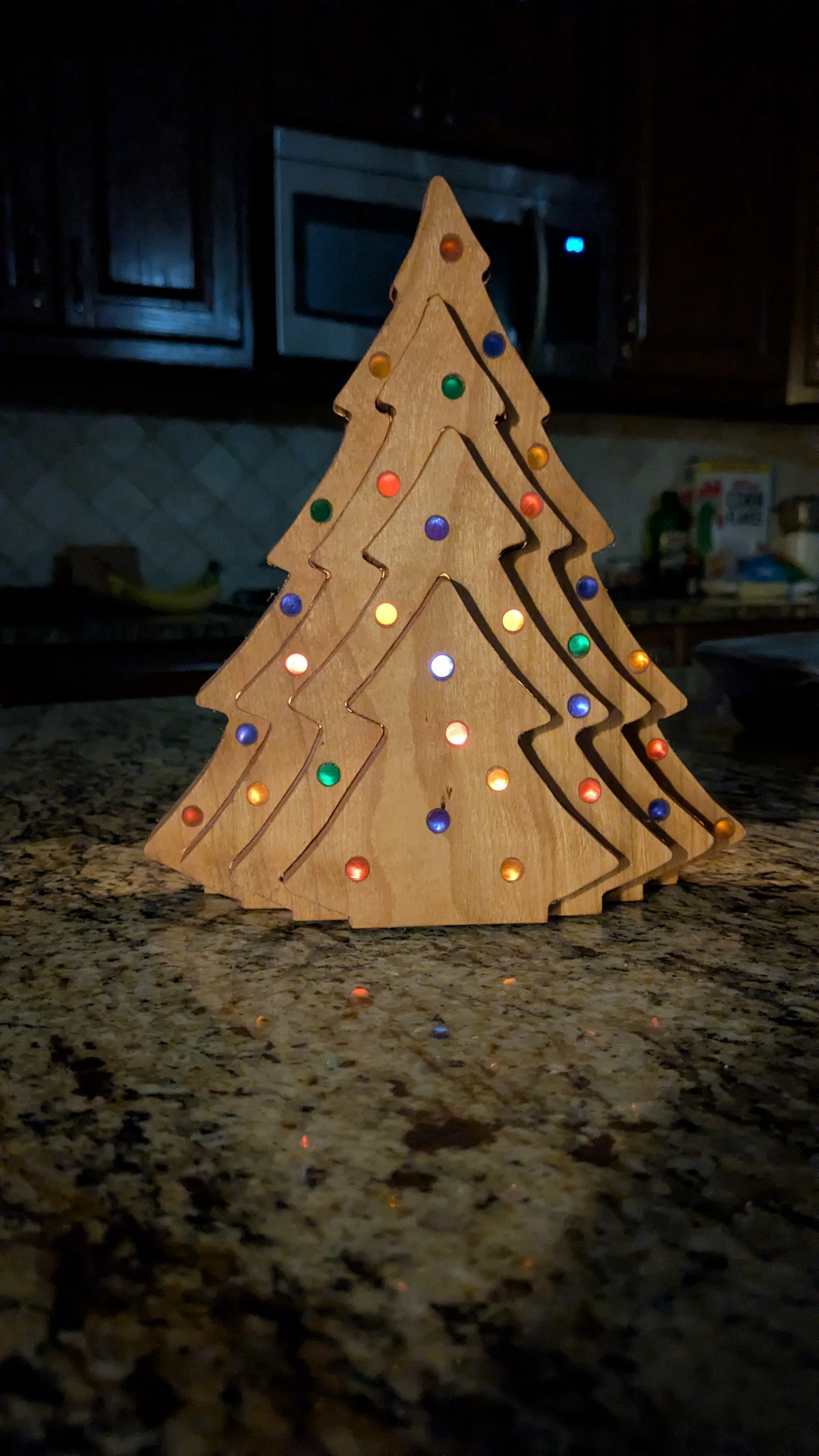 Wooden Christmas tree decoration with colorful lights, placed on a kitchen countertop.