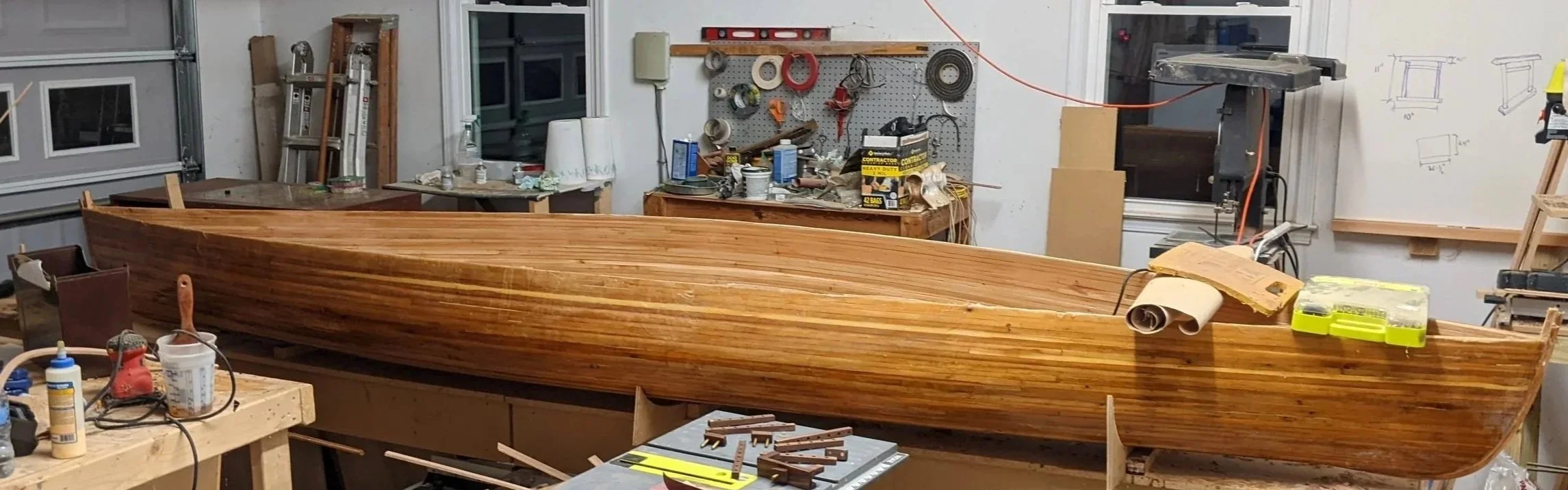Wooden boat being built in a woodworking shop with various tools and materials around.
