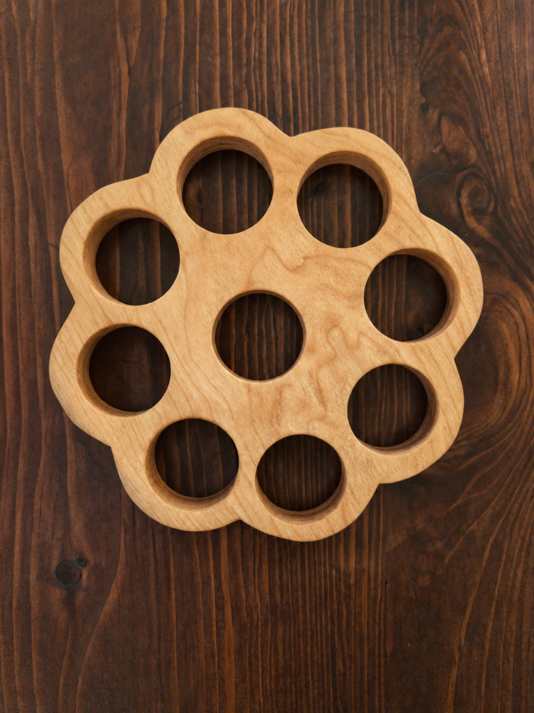 A wooden finger ring holder with eight circular slots, placed on a wooden surface.