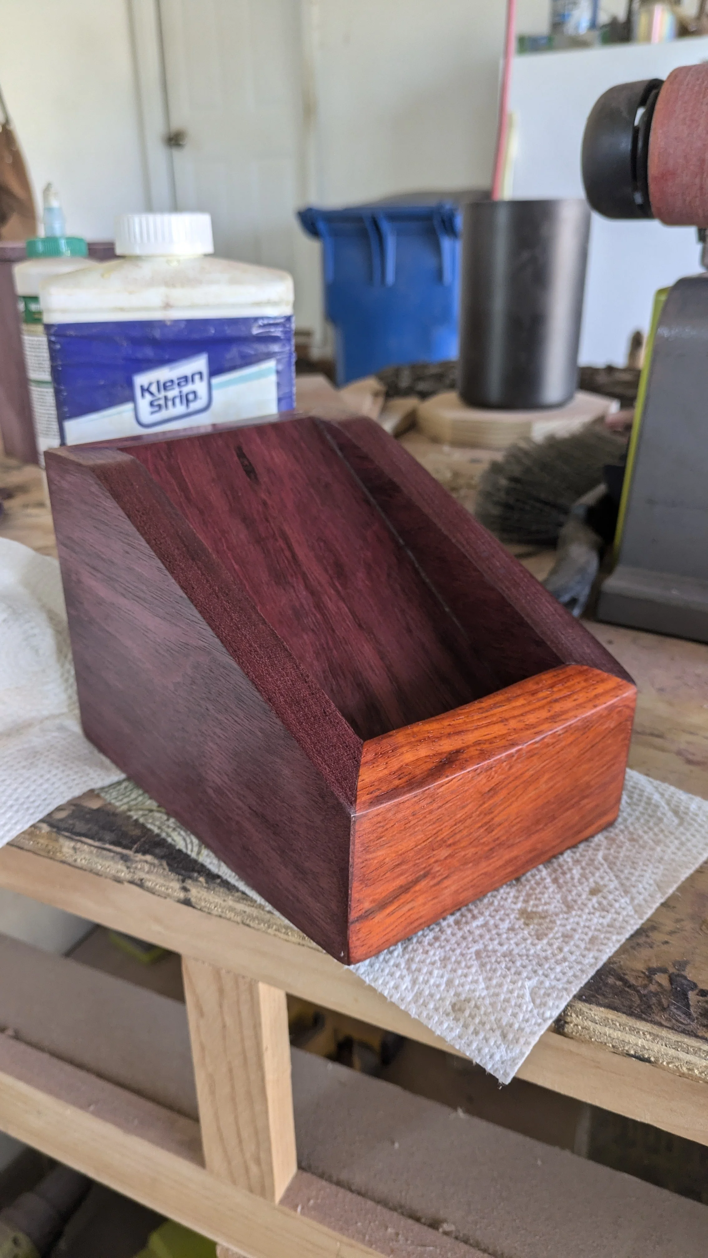 A wooden box with a reddish finish placed on a workbench in a woodworking shop.