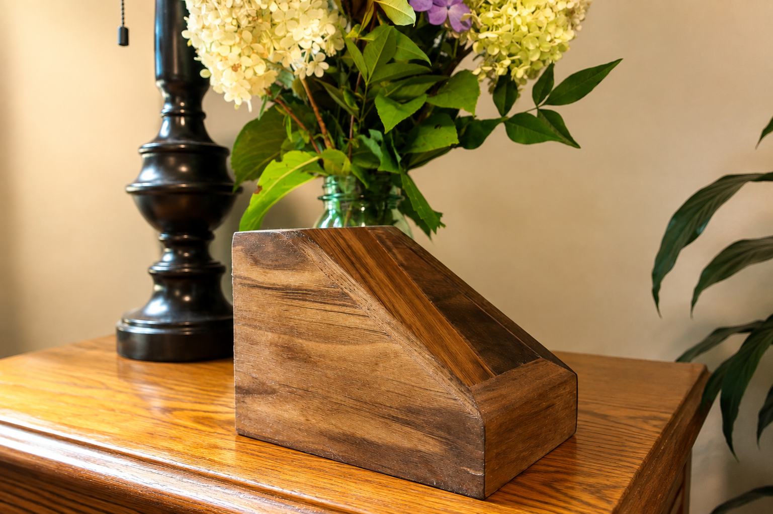 Wooden napkin holder on a polished wooden table, with a black lamp and a vase of white and purple hydrangeas in the background.