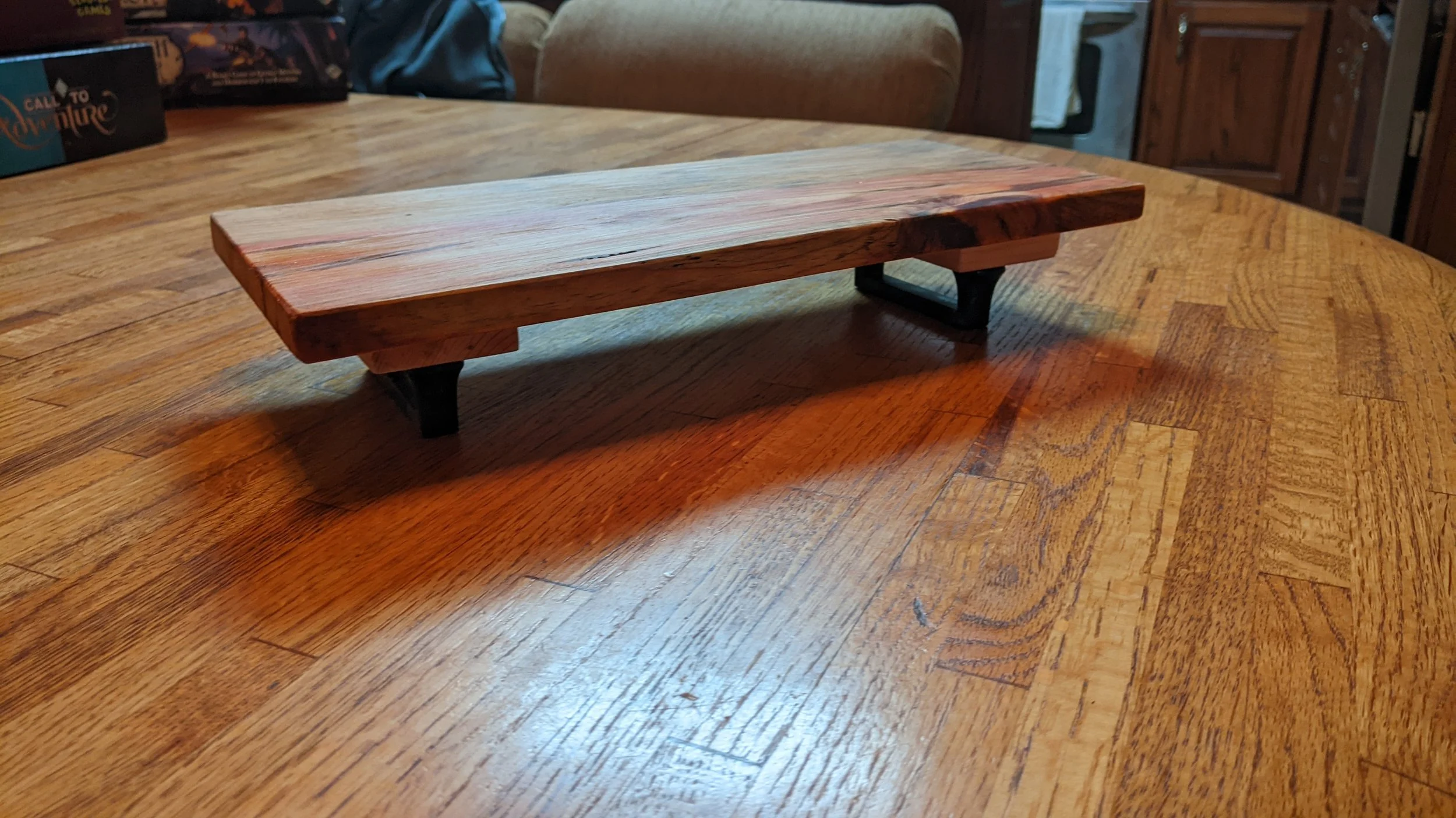 A small rectangular wooden shelf with metal legs on a wooden table in a cozy room.
