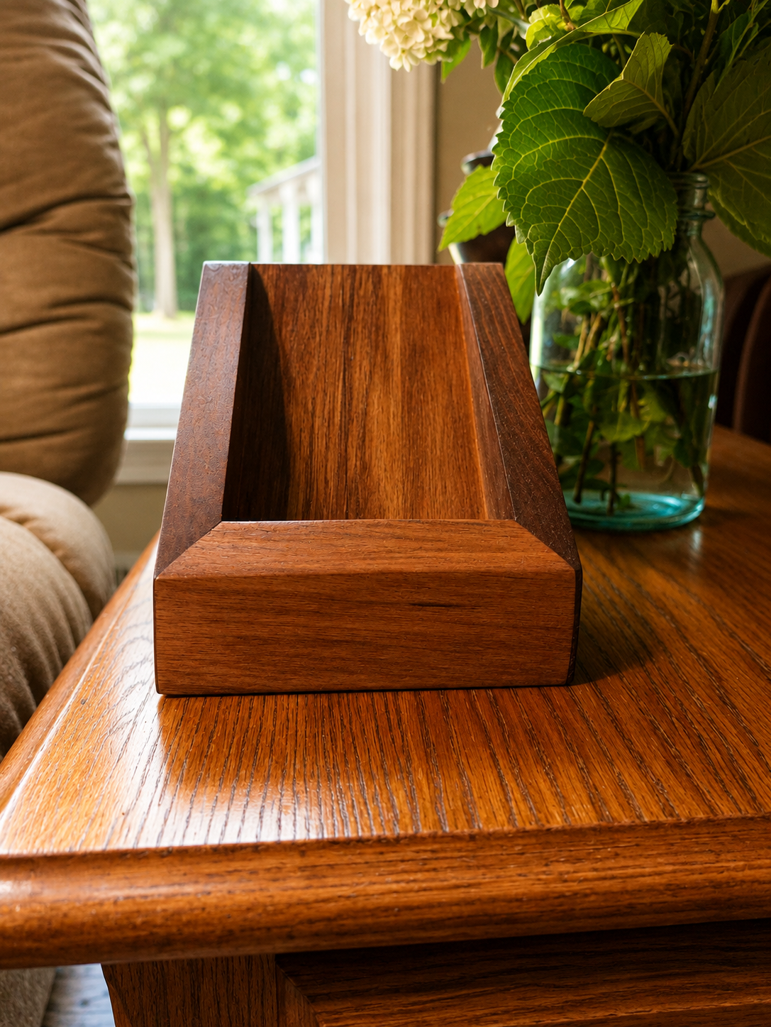 Wooden letter holder on a wooden table with a vase of green leaves and white flowers in the background.
