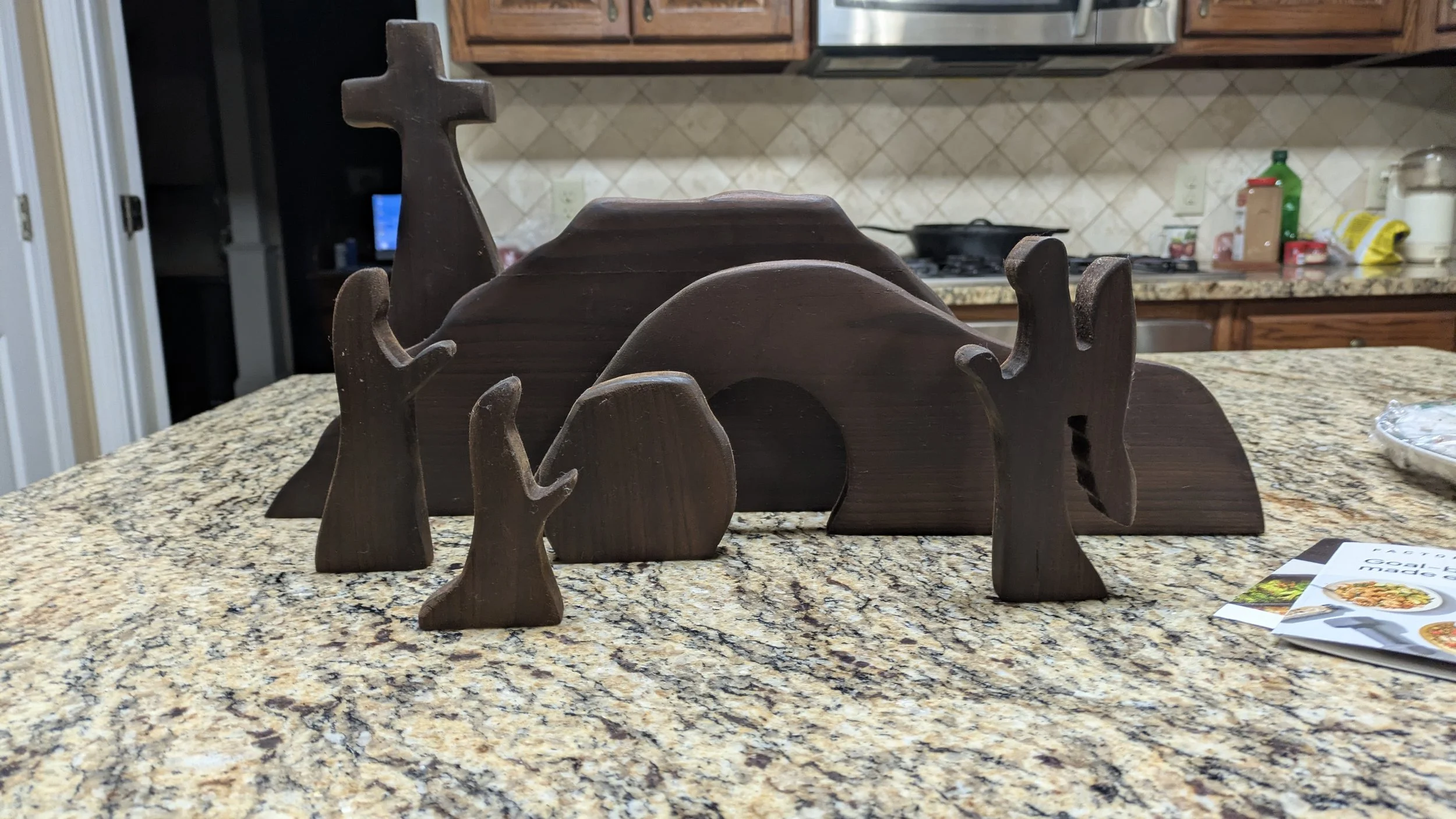 Decorative wooden figurines of animals arranged on a granite kitchen countertop, with kitchen cabinets and appliances in the background.