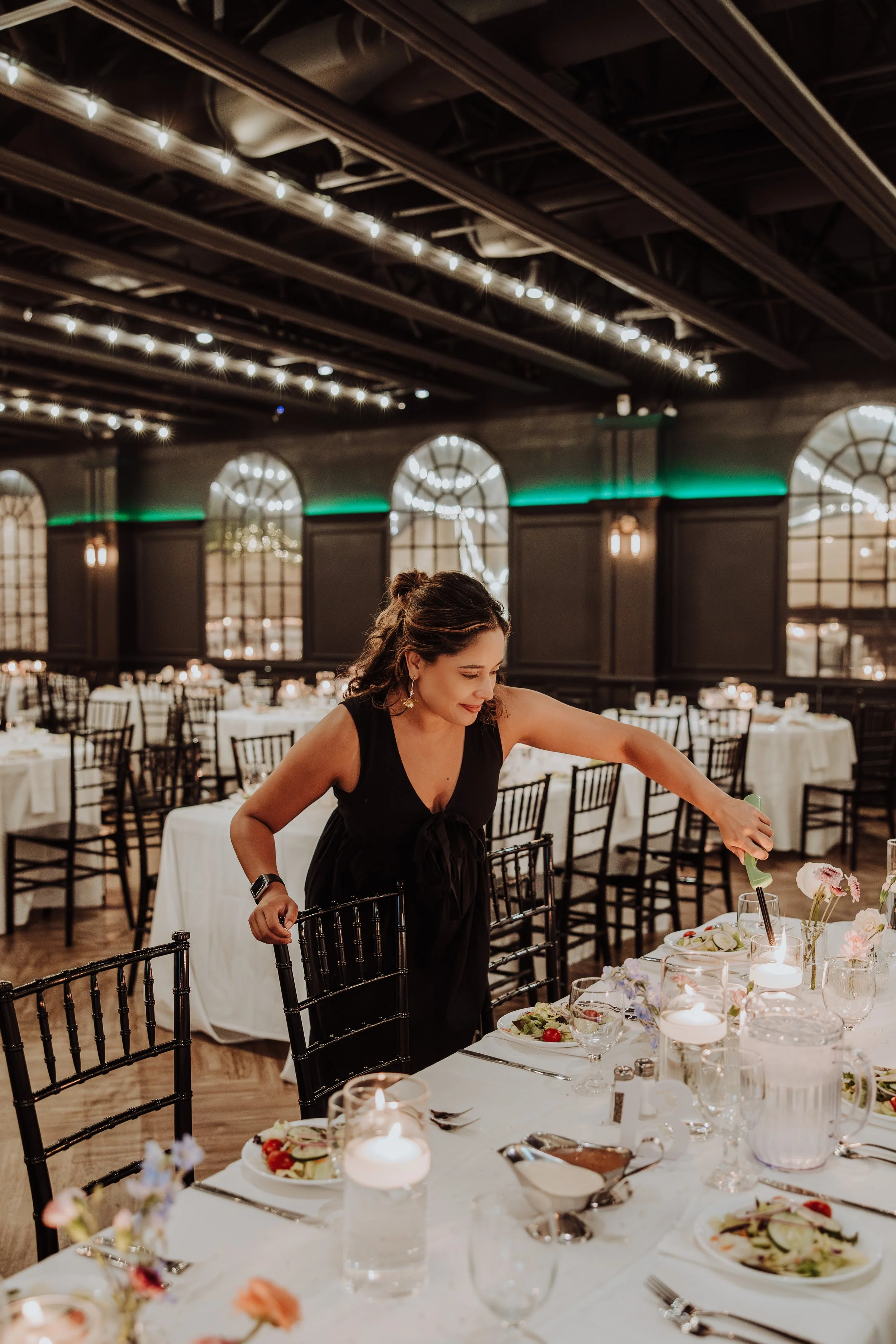 A professional wedding coordinator adjusting candles and floral centerpieces on a reception table at a luxury indoor venue space in Portugal