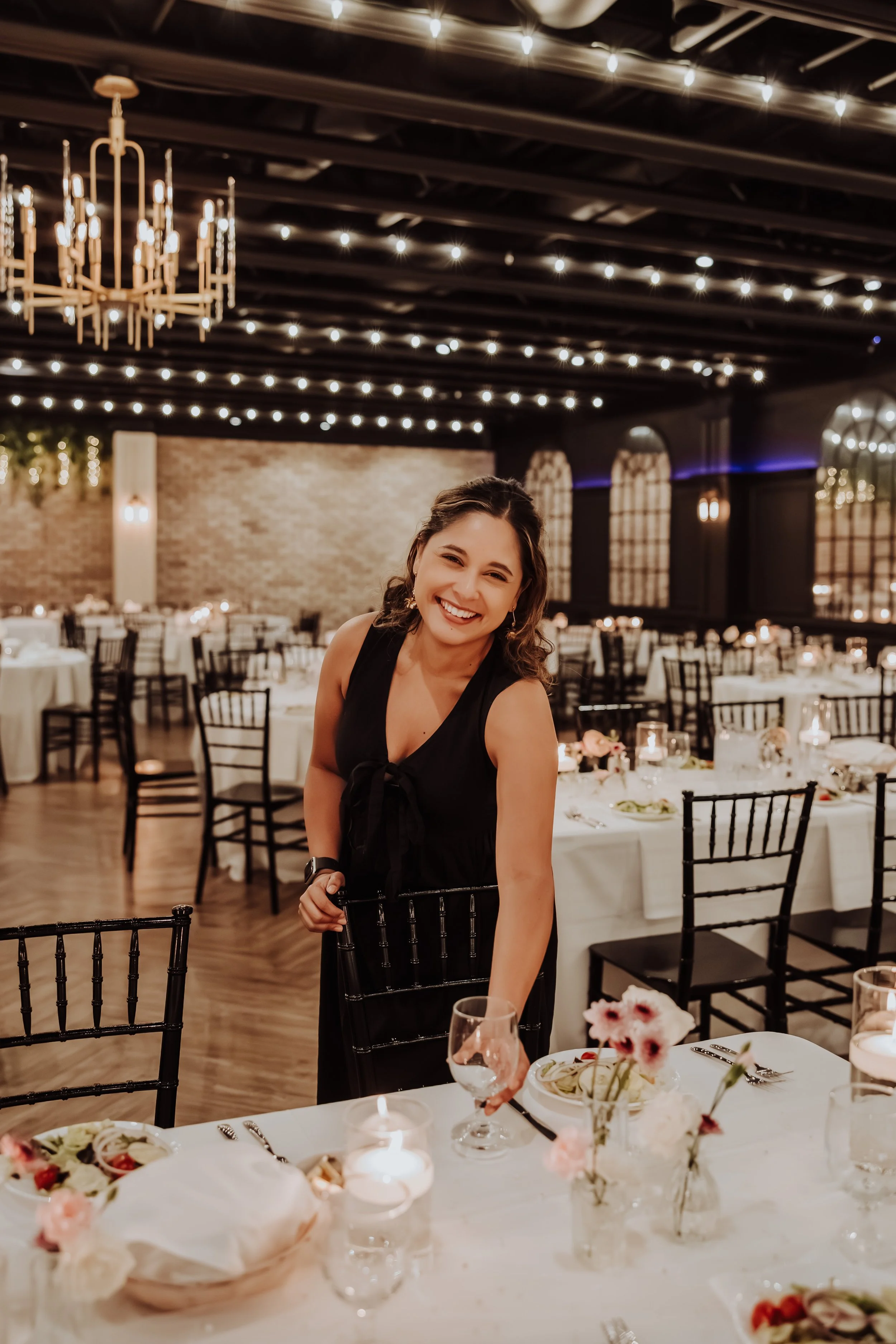 Sabryna Cisneros, founder of The Portugal Bride Co., smiling while setting up tables and coordinating a wedding reception under string lights