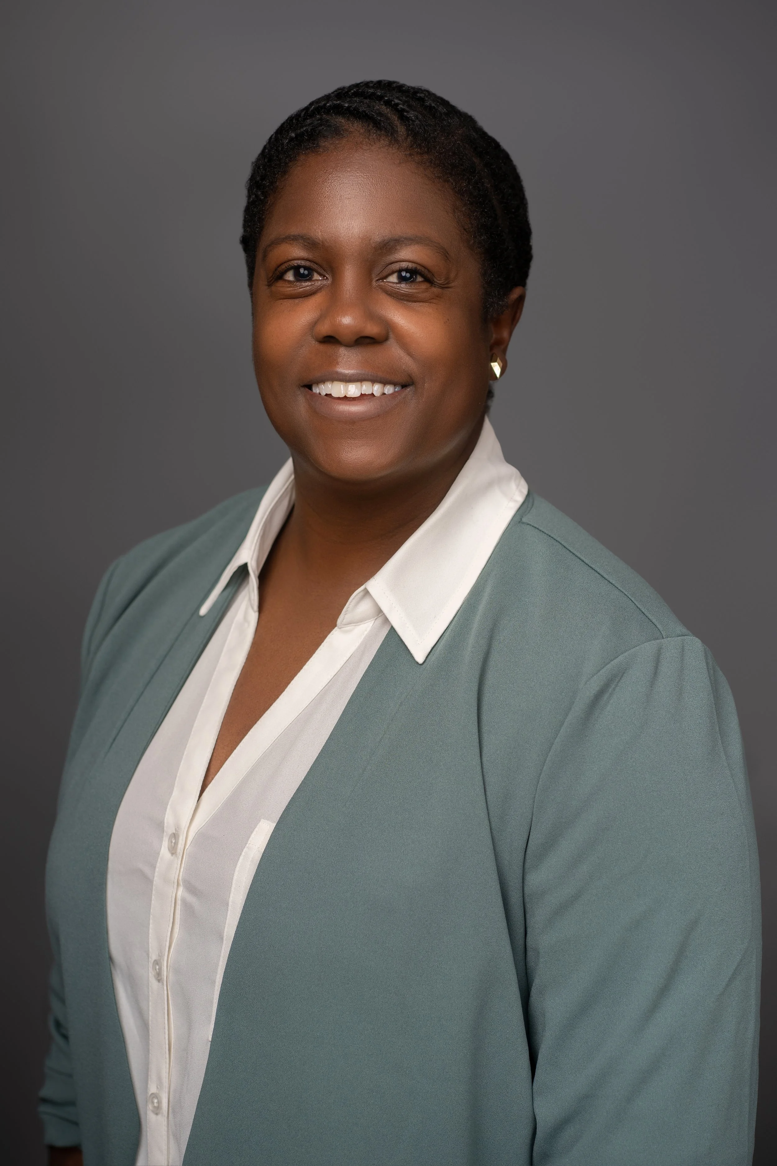 A professional woman with short hair, wearing a white blouse and light green blazer, smiling in front of a gray background.