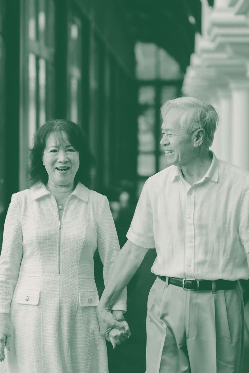 A happy elderly couple holding hands and smiling while walking together in a modern, glass-enclosed building.
