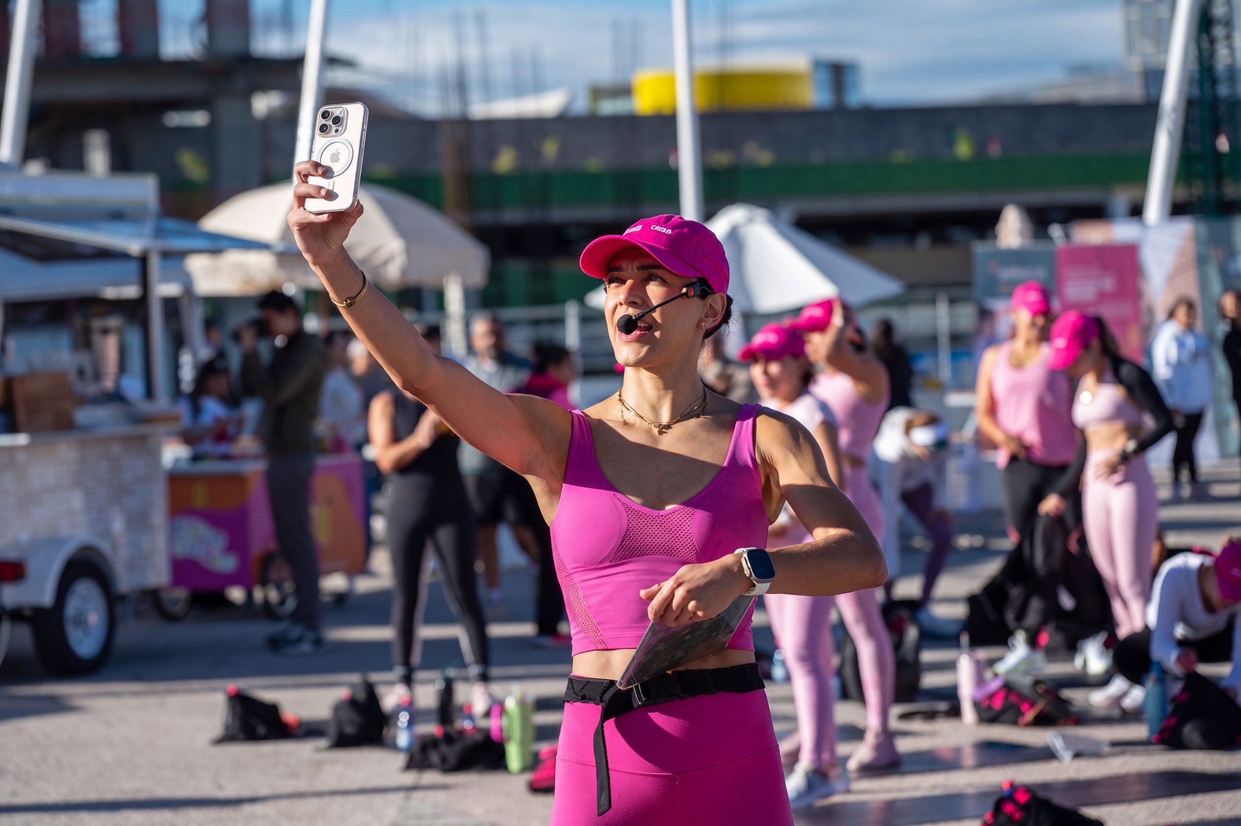 Mujer dirigiendo clase fitness al aire libre con participantes en ropa deportiva rosa, fotografía de evento por Carlos Vega.