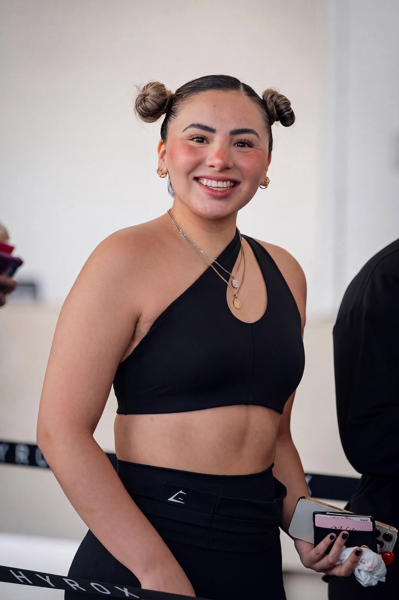 Mujer en ropa deportiva sosteniendo celular y toalla, retrato fitness por Carlos Vega en Hyrox Puebla.