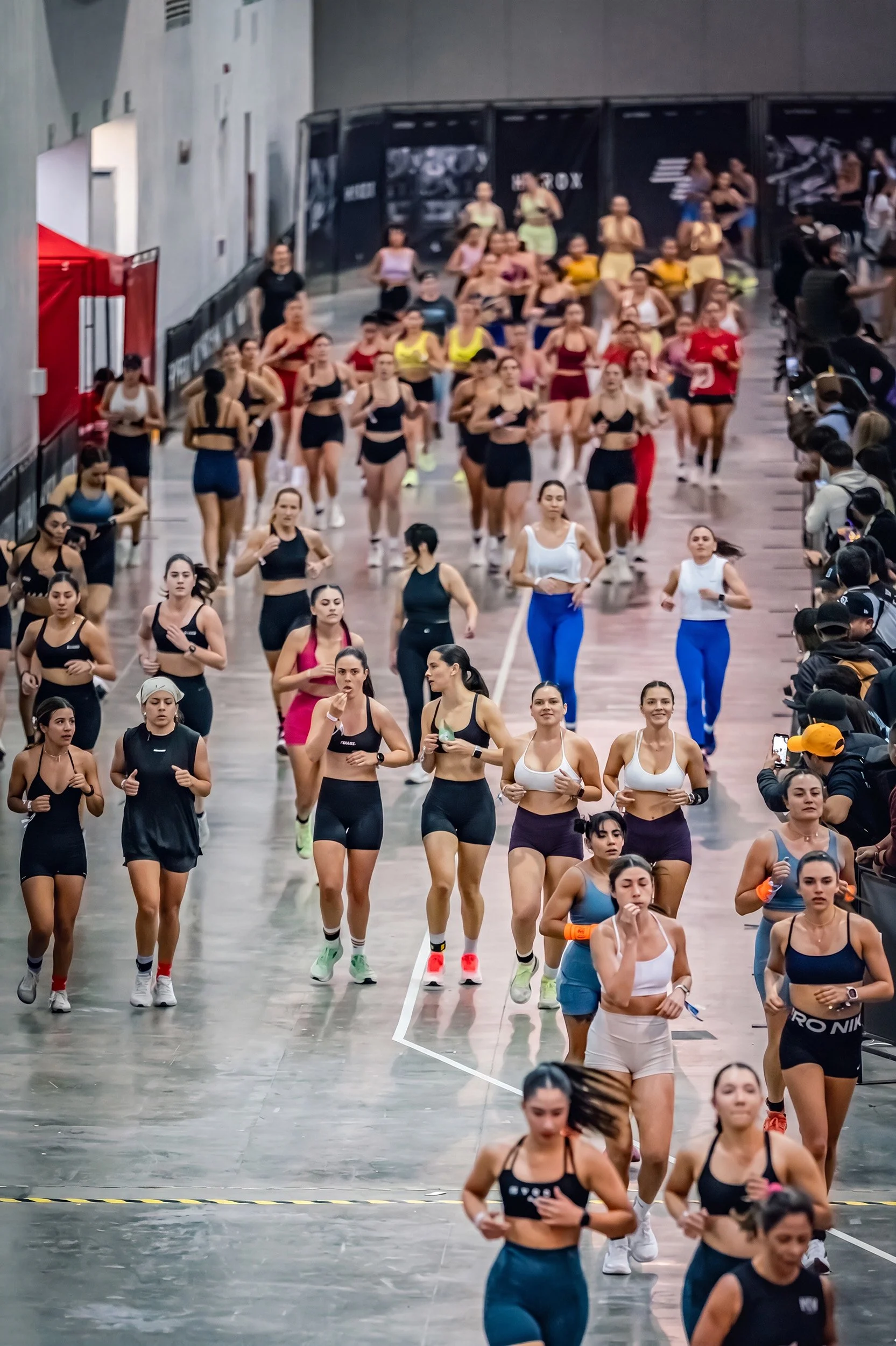 Grupo de mujeres corriendo en pista interior durante competencia fitness, fotografía deportiva por Carlos Vega en Hyrox Puebla.